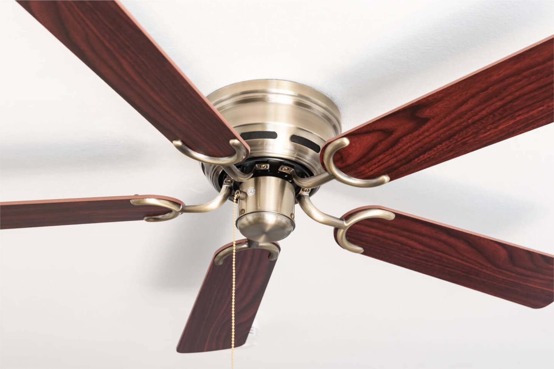 Deckenventilator mit braunen Flügeln, Messing-Finish und Zugkette vor weißer Decke.