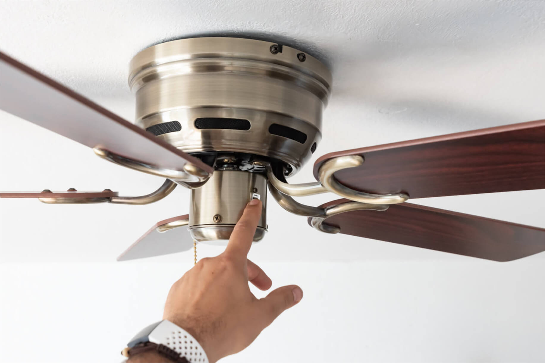 Eine Hand drückt einen Knopf an einem Deckenventilator, der an einer weißen Decke befestigt ist.