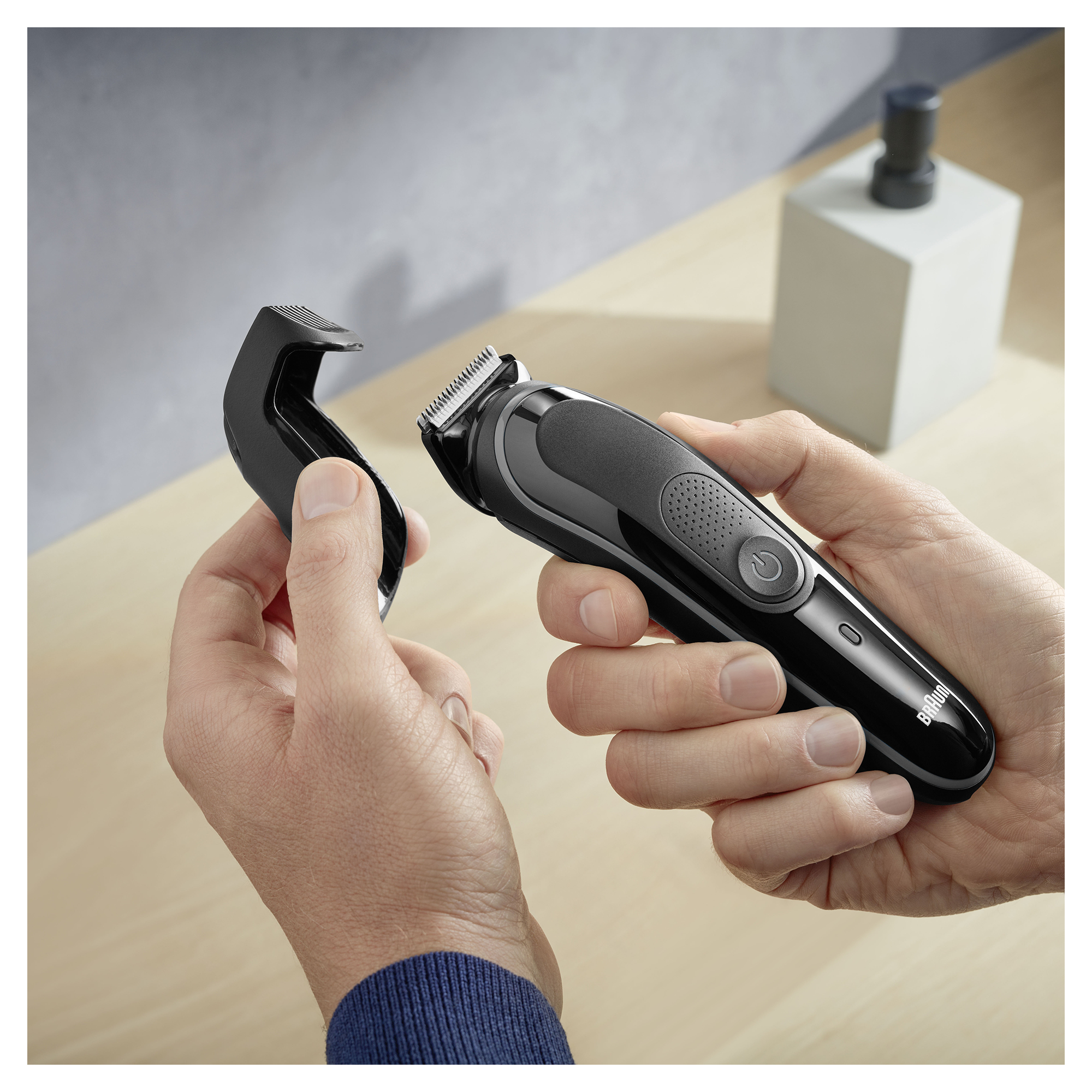 Dłonie trzymające czarną i szarą trymer do brody z ostrzem.