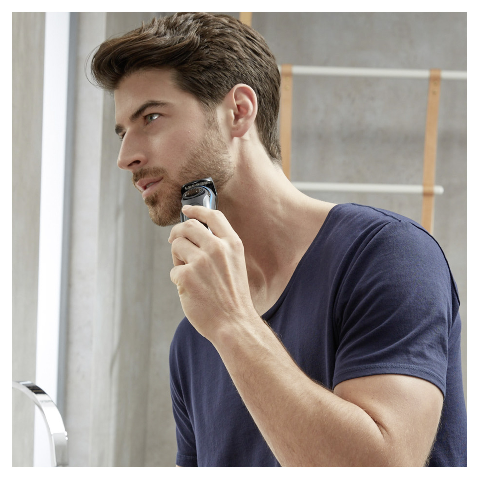 Mężczyzna goli brodę golarką elektryczną przed lustrem.