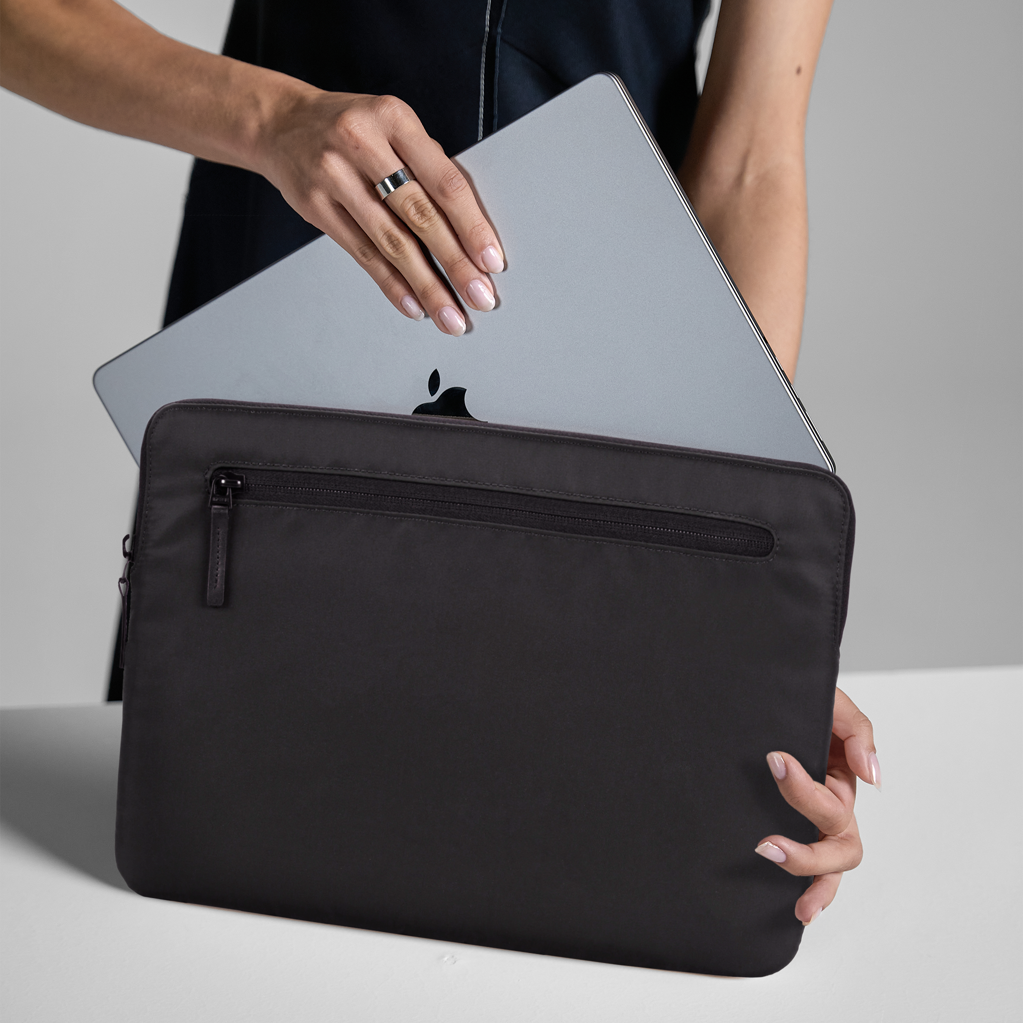 Una persona tiene un laptop nero in una custodia nera, su una superficie bianca.