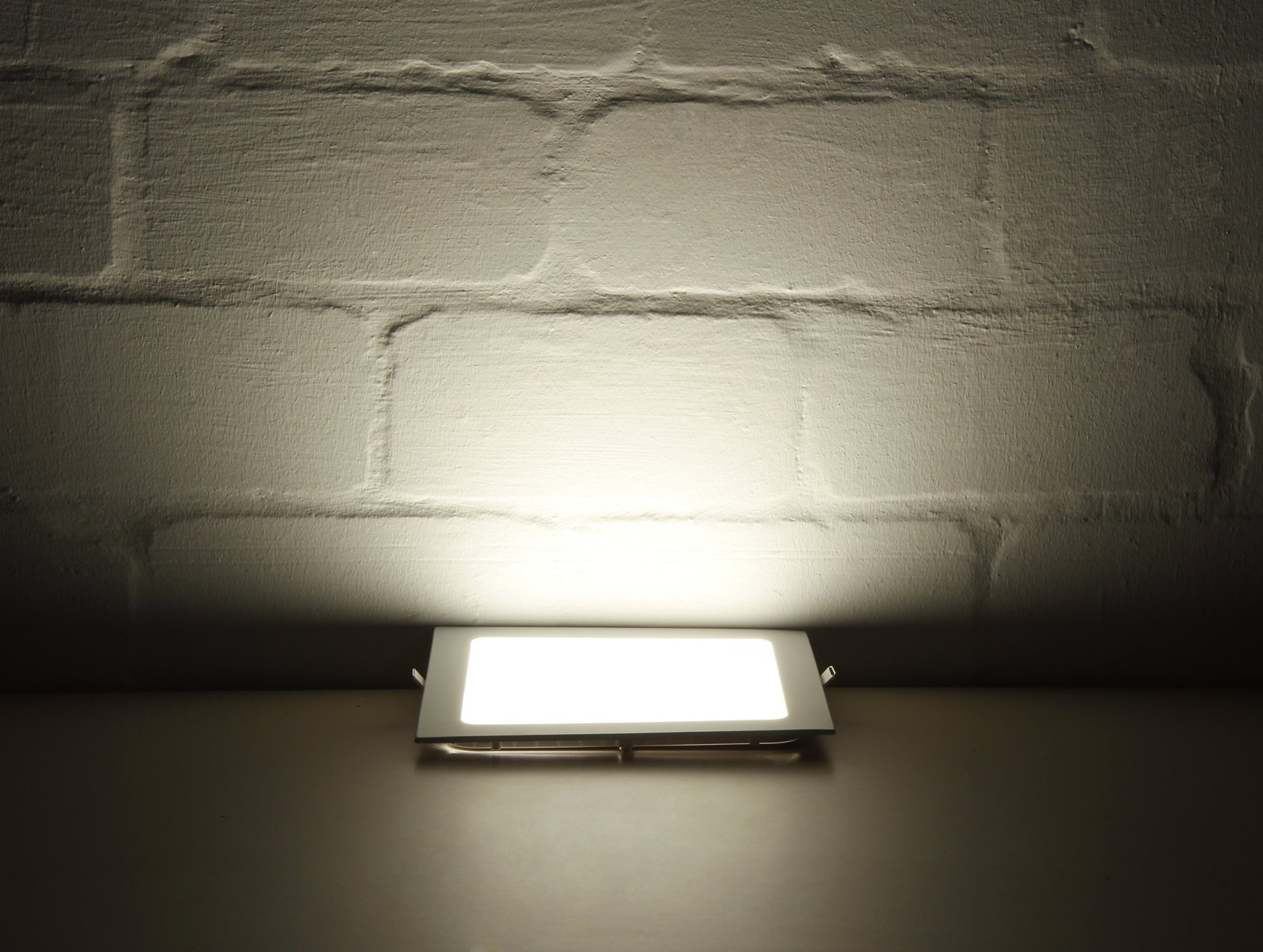 Helles LED-Licht scheint aus einer Einbauleuchte an einer weißen Backsteinmauer.