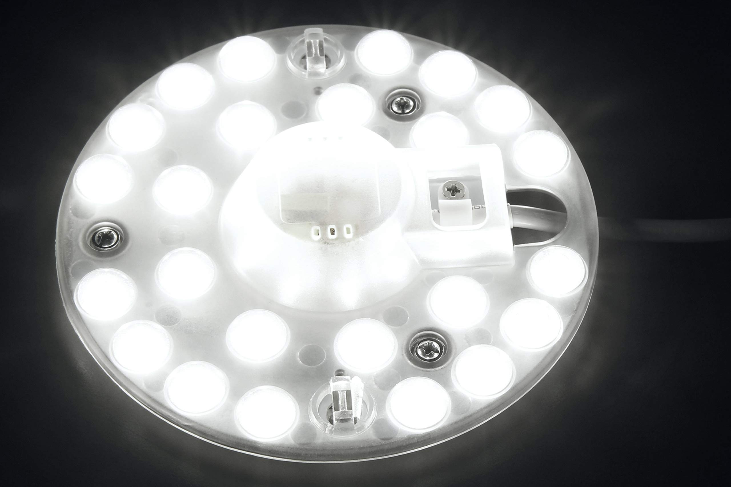 Runde LED-Leuchte mit vielen kleinen weißen Lichtern auf weißer Oberfläche, vor dunklem Hintergrund.
