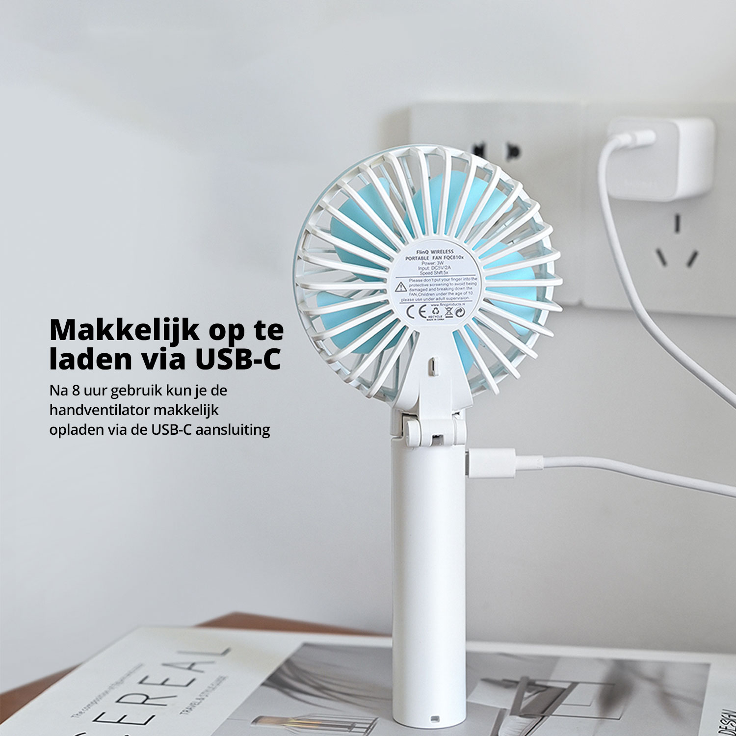 A white and blue portable fan is plugged into a wall outlet via USB-C.