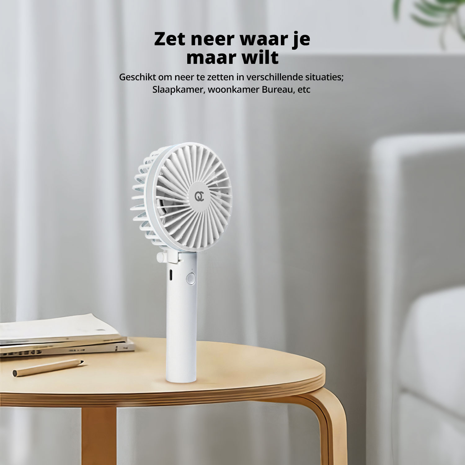 Een witte draagbare ventilator staat op een klein houten tafeltje, naast boeken en een potlood in een gezellige kamer.