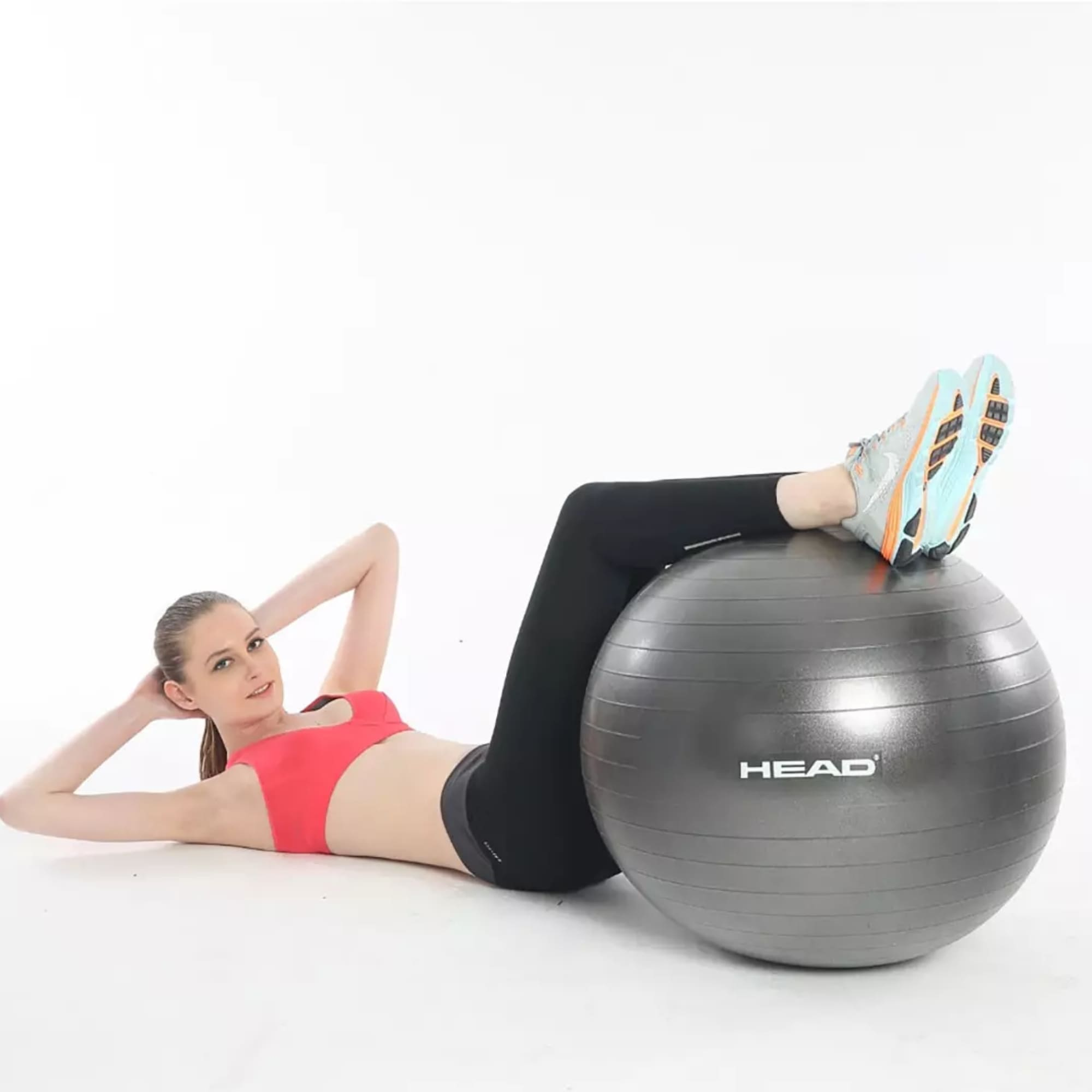 Donna che si esercita con una palla da ginnastica grigia, indossa un reggiseno sportivo rosso e leggings neri.