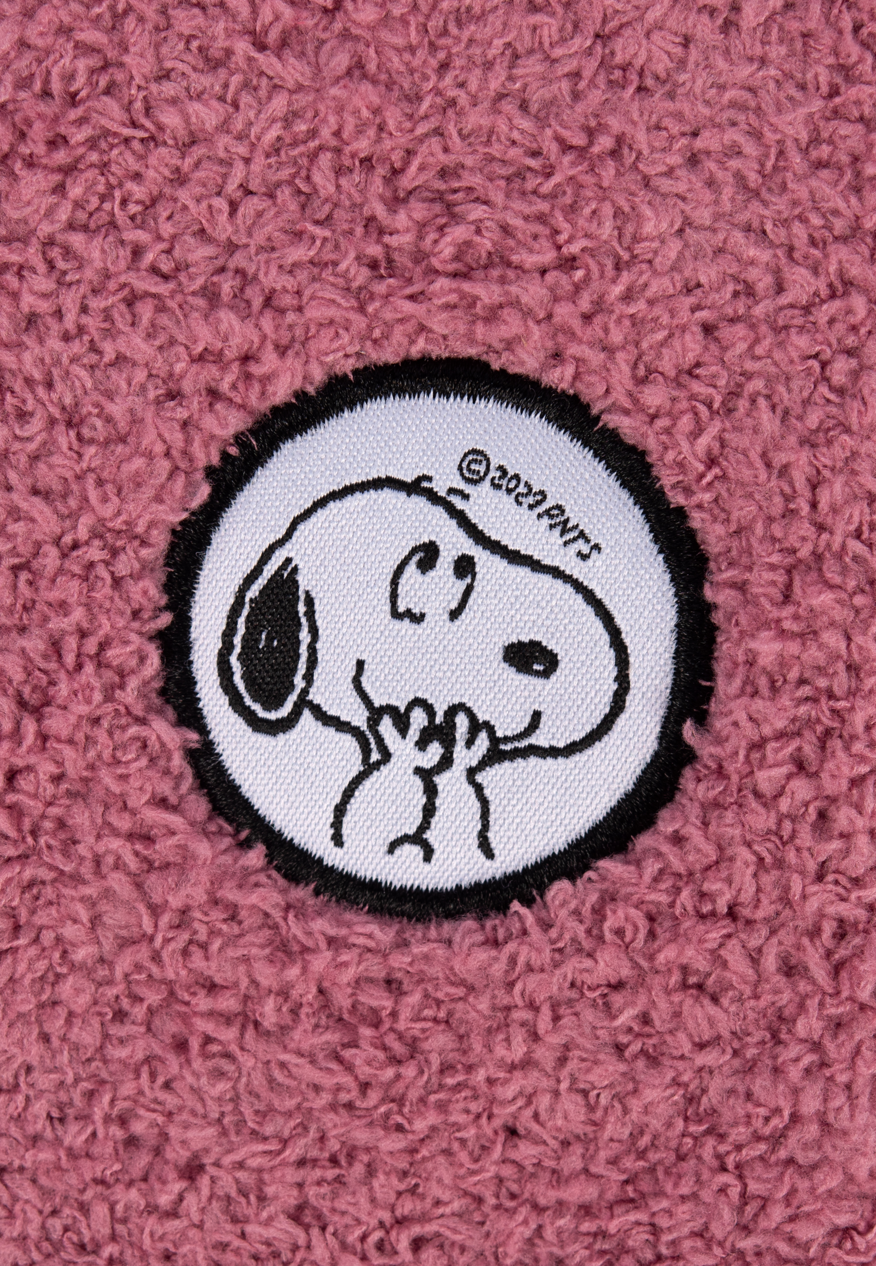Nahaufnahme eines Snoopy-Aufnähers auf einem flauschigen rosa Hintergrund.