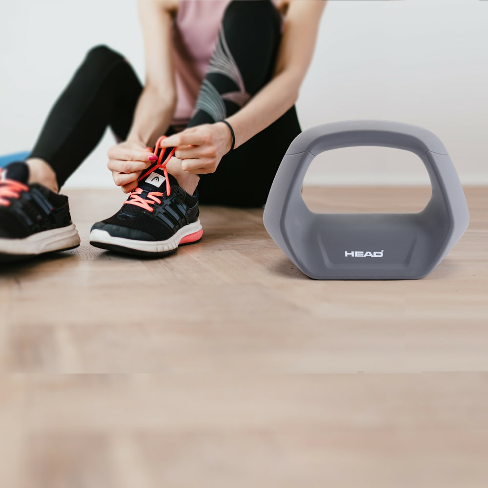 Vrouw die veters strikt met een grijze kettlebell rechts. Zwarte schoenen en leggings.