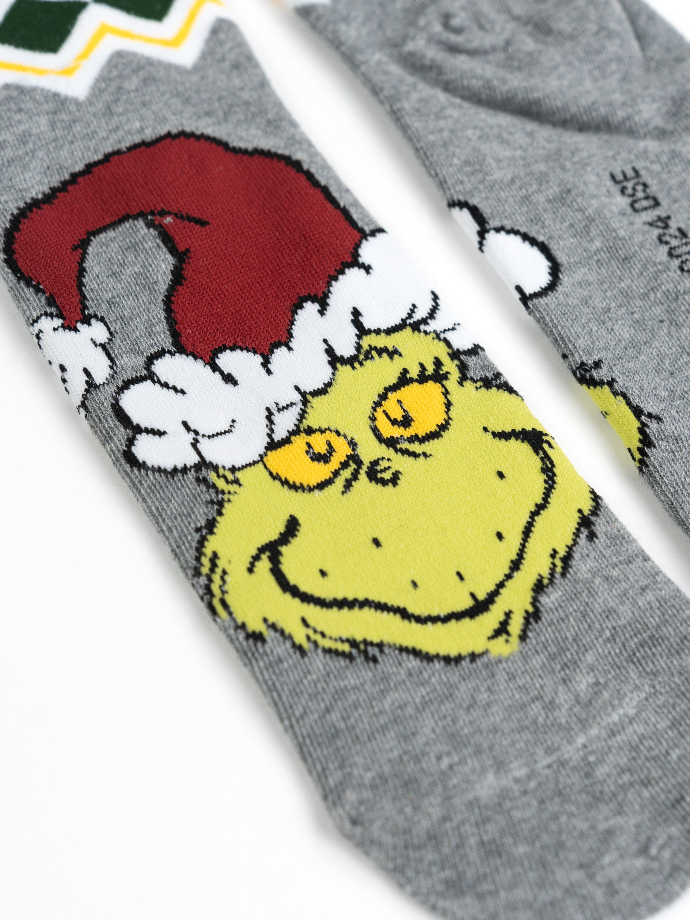 Ein Paar graue Socken mit Grinch-Gesichtern und einem Weihnachtsmannhut. Weißer Hintergrund.