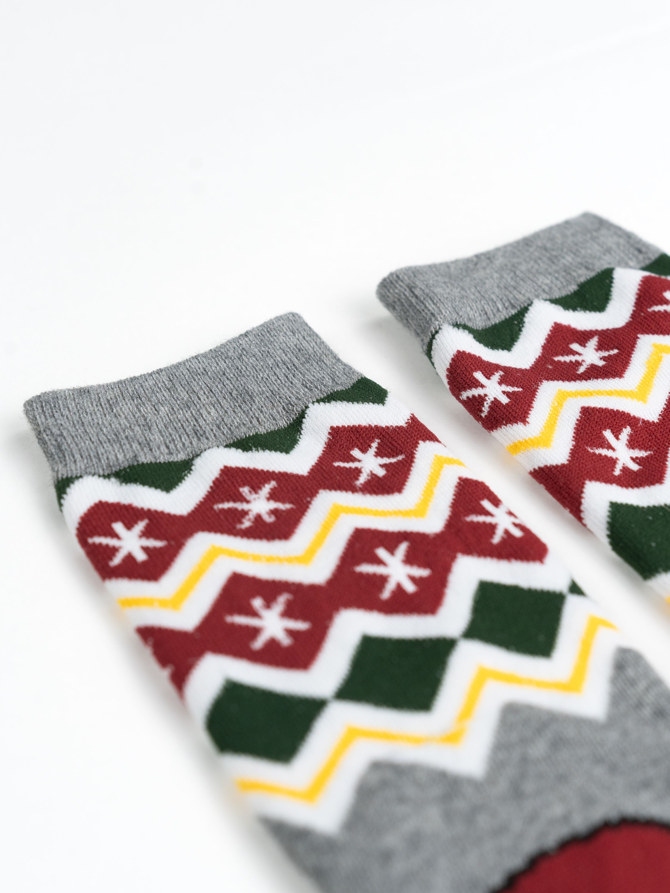 Zwei Socken mit grauem Bund und Zehen. Das Hauptmuster ist Zickzack mit Schneeflocken und grünen Rauten.