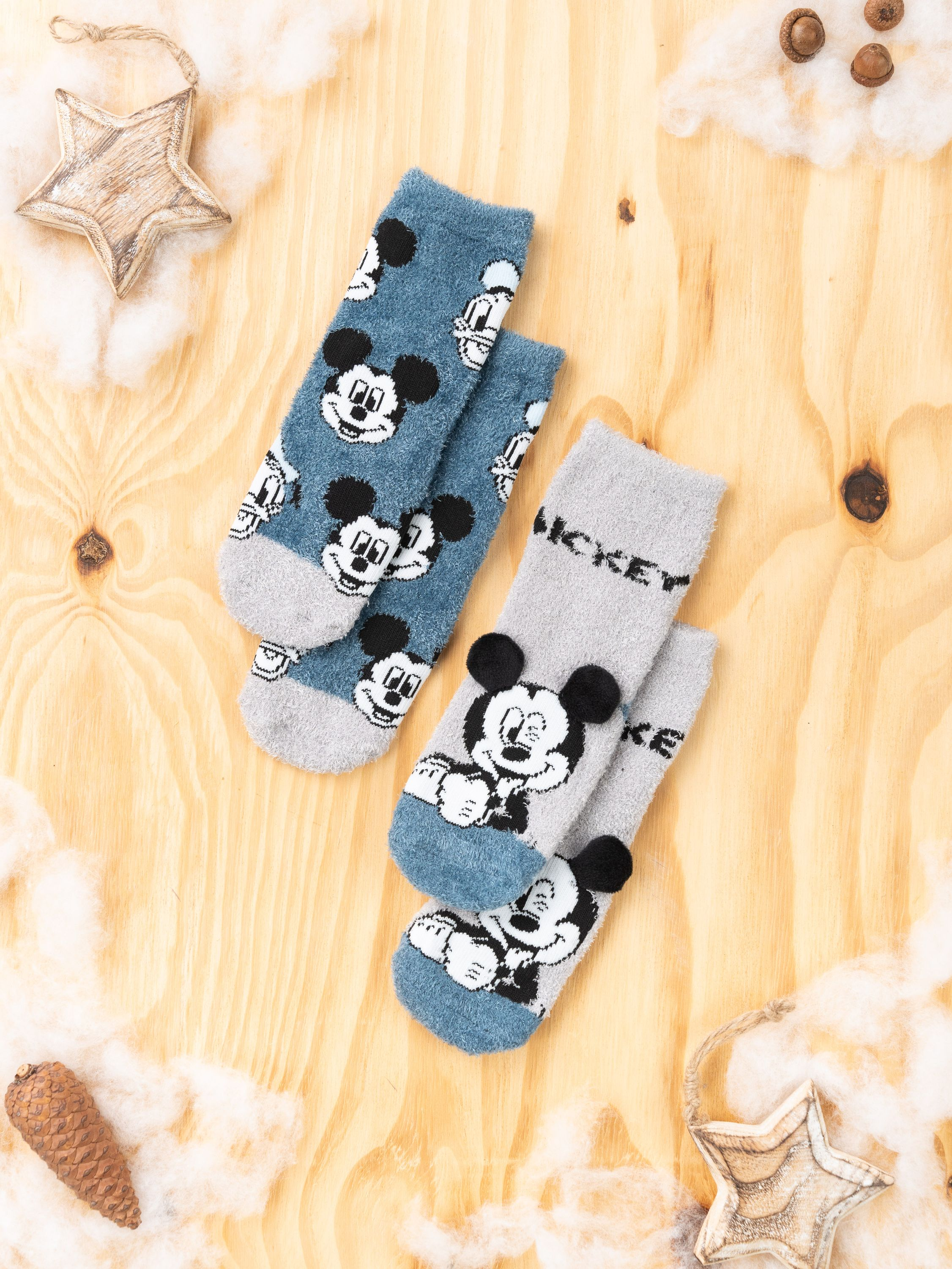Zwei Paar Mickey Mouse Socken auf einer Holzoberfläche, mit dekorativen Elementen wie Sternen und Watte.