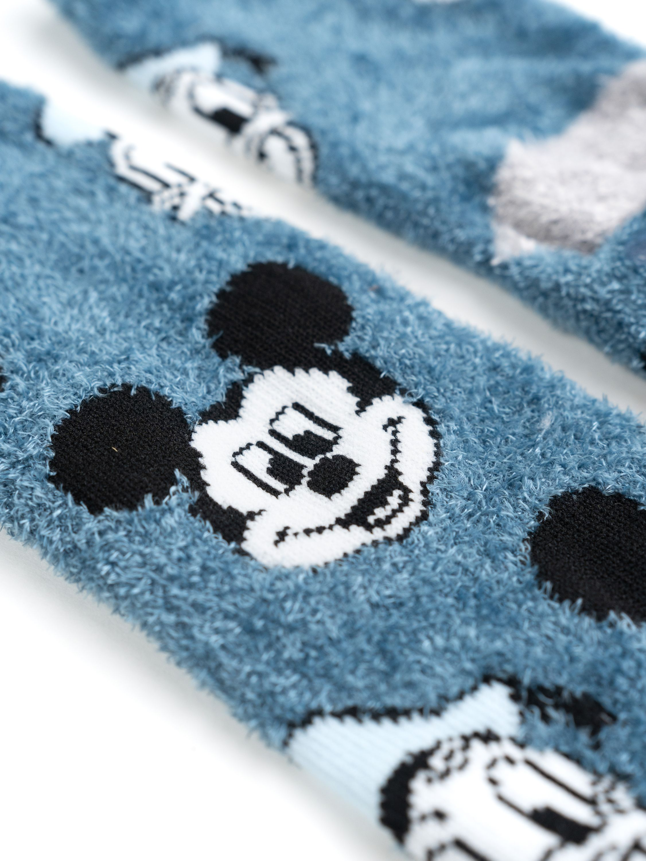 Mickey Mouse Socken mit blauem, flauschigem Muster. Weißer Hintergrund. Schwarz-weißes Mickey Gesicht.