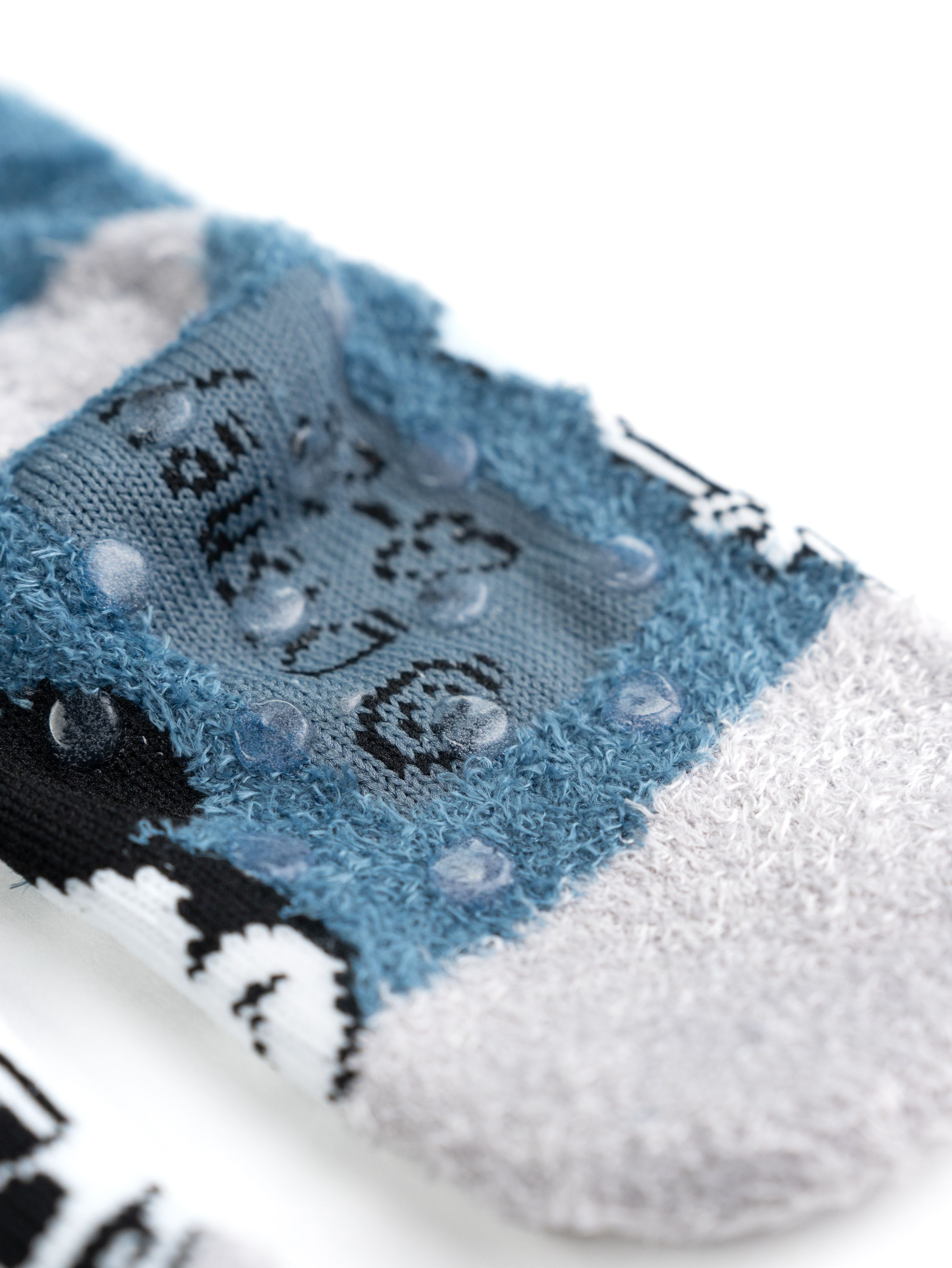 Nahaufnahme der Socken-Sohle. Grau und blau mit transparenten, kreisförmigen Grip-Pads. Weißer Hintergrund.