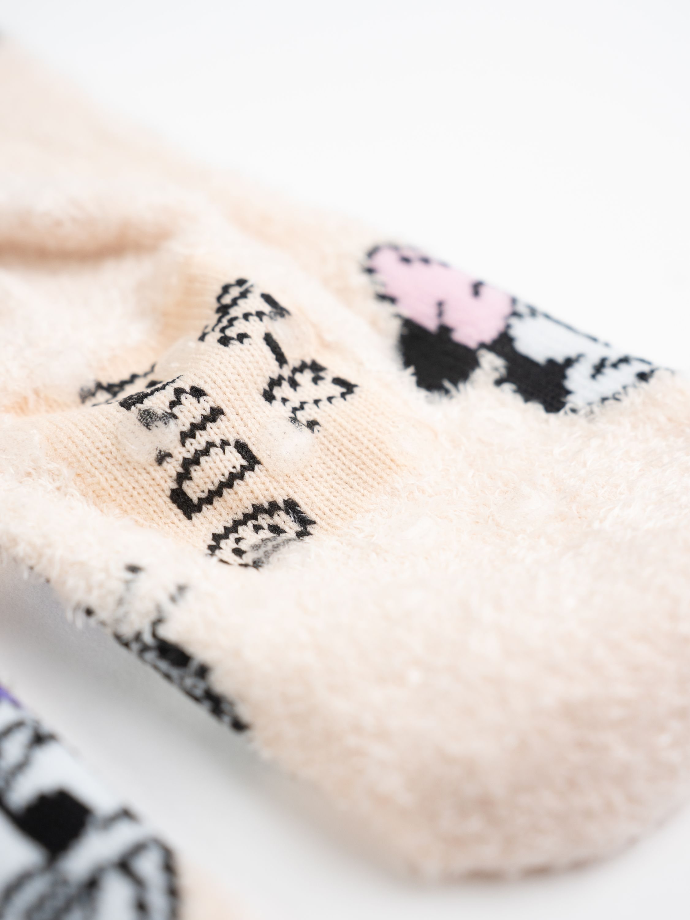 Nahaufnahme eines Paares weicher, hellbeiger Socken mit schwarzen und rosa Designs. Weißer Hintergrund.