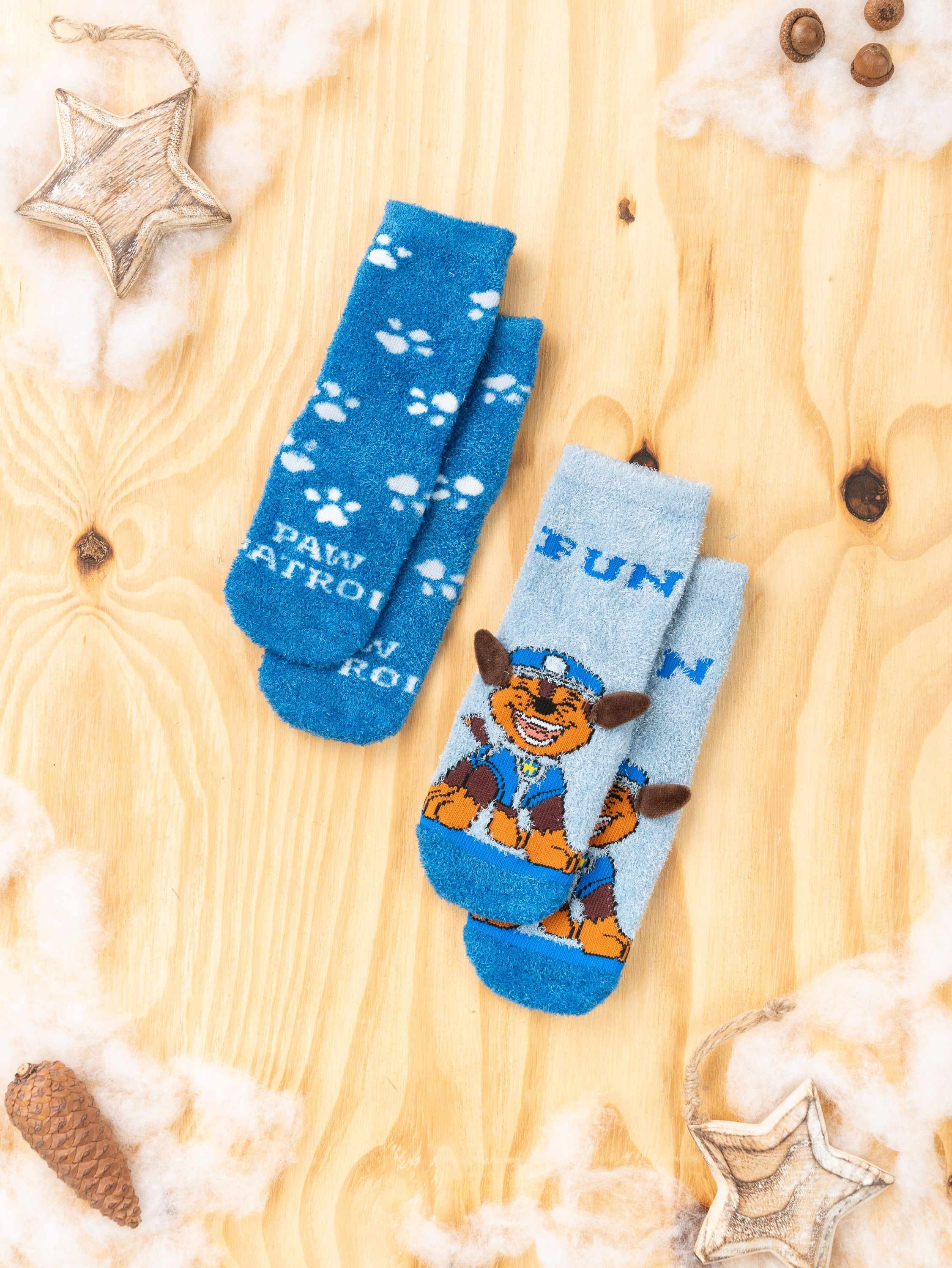 Zwei Paar Paw Patrol Socken auf einer Holzoberfläche mit dekorativen Elementen.