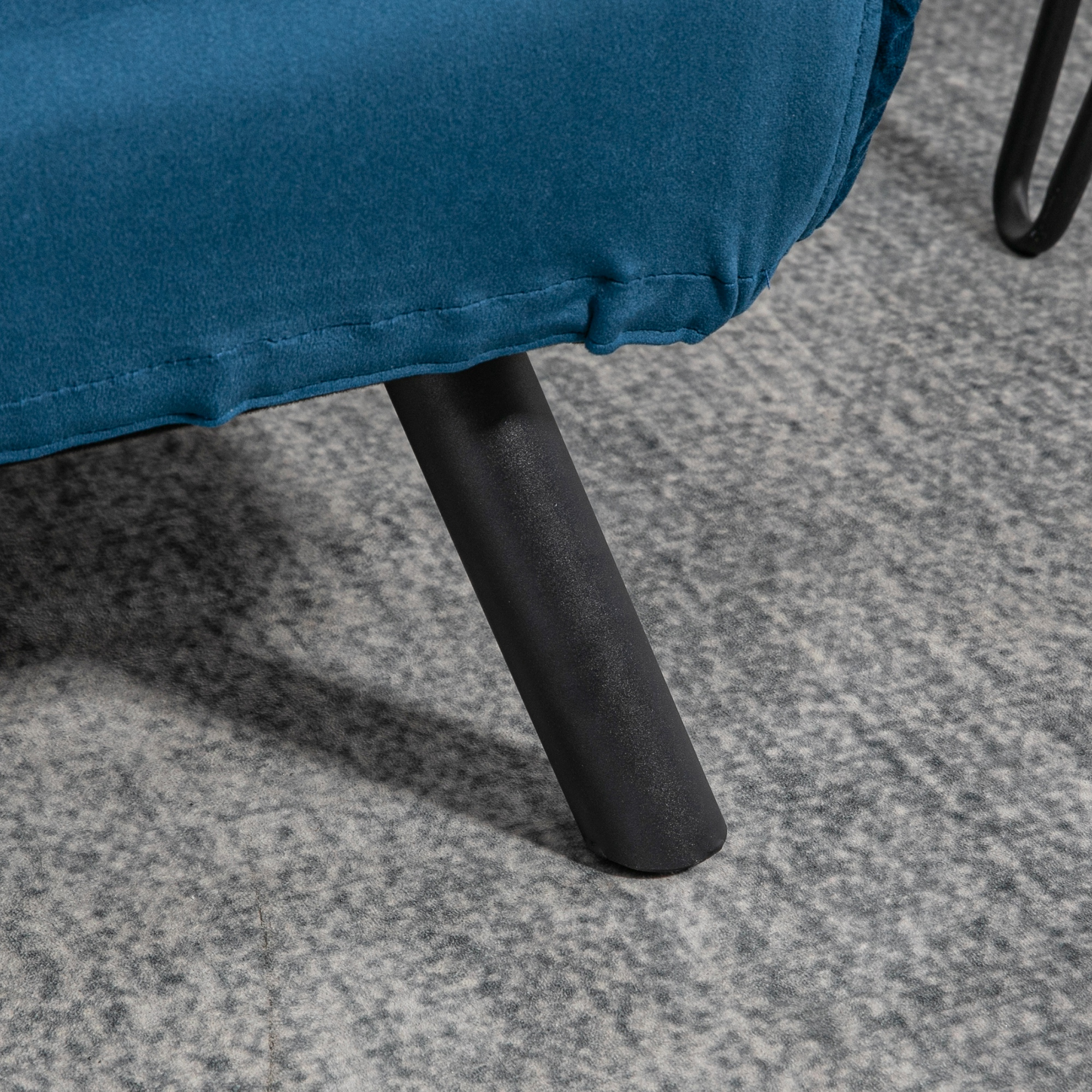 Primer plano de una pata de sofá verde azulado sobre una alfombra gris. La pata es negra y cilíndrica.