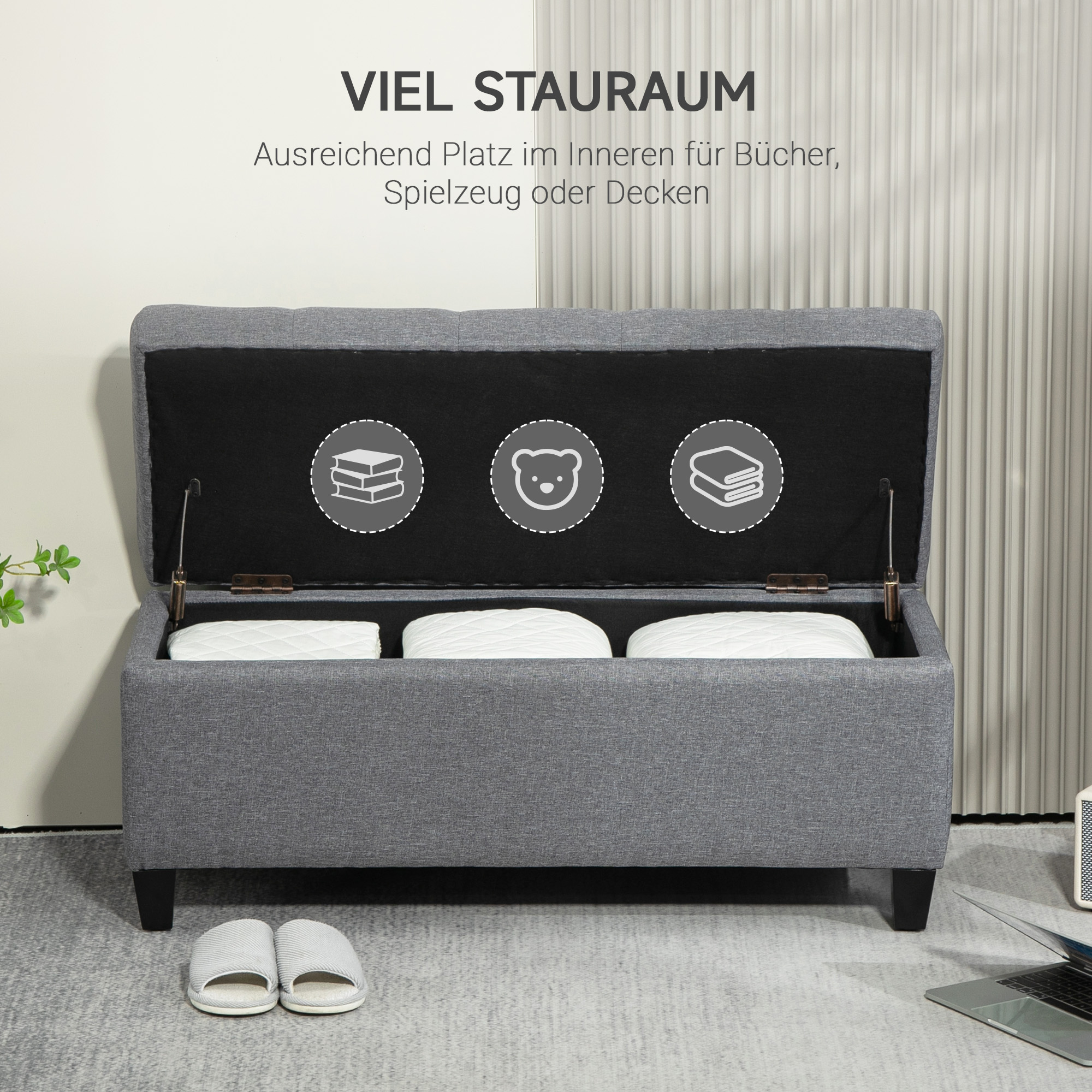 Graue Aufbewahrungsbank mit offenem Deckel, der Stauraum mit drei weißen Kissen zeigt.