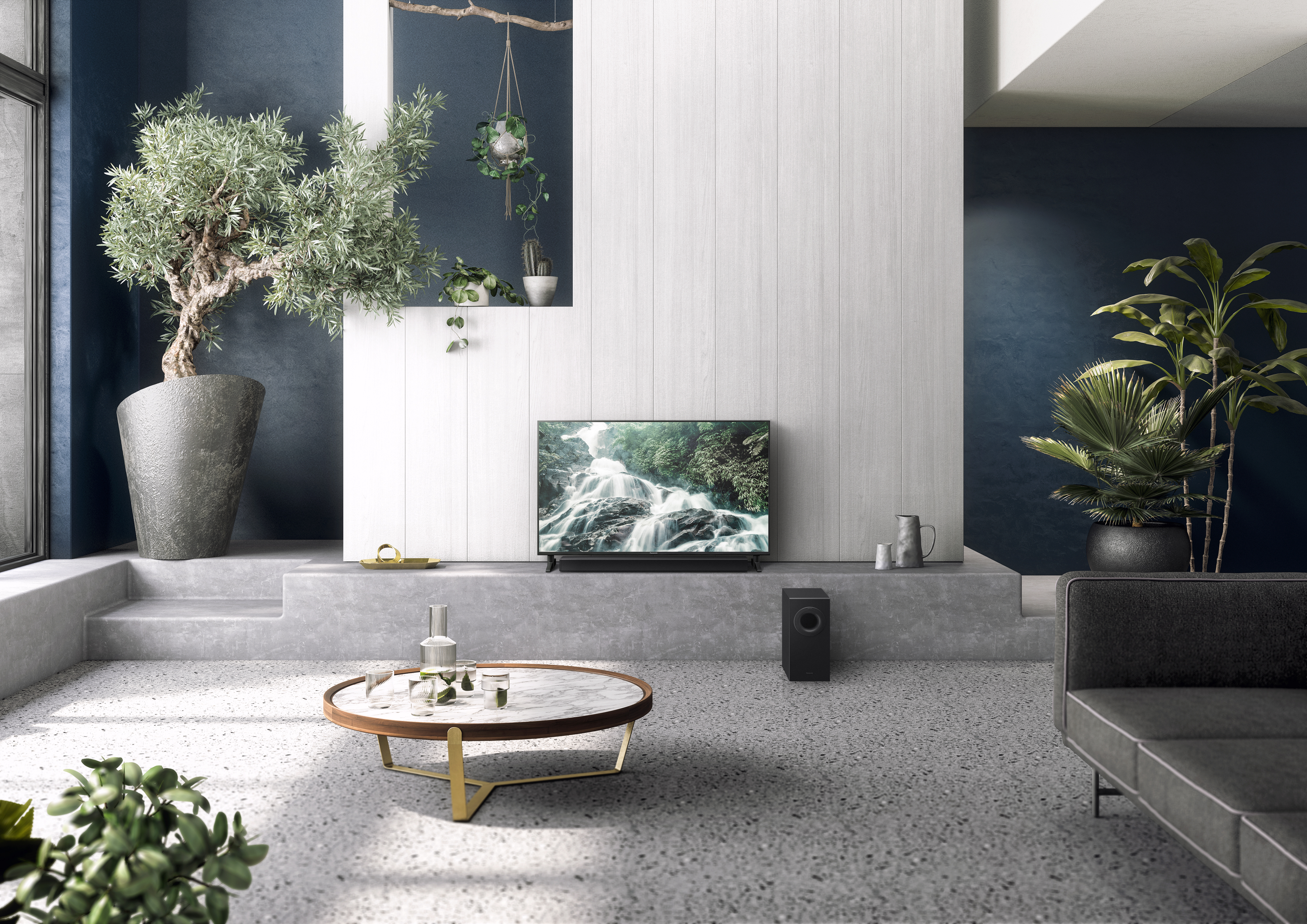 Salon z telewizorem, okrągłym stołem, sofą i roślinami. Szara podłoga i ciemnoniebieska ściana.