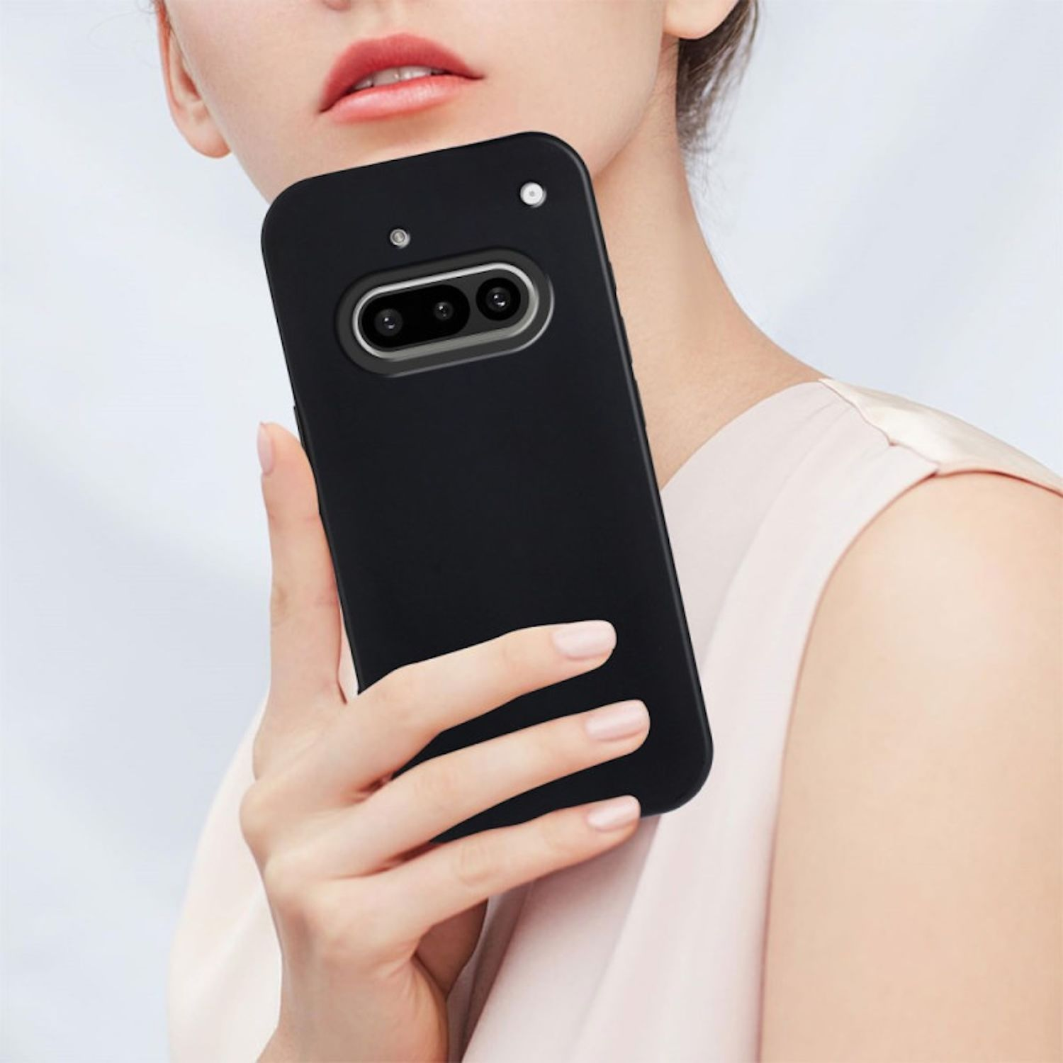 Una mujer sosteniendo un teléfono negro con una protuberancia de cámara. Usa un top rosa claro.