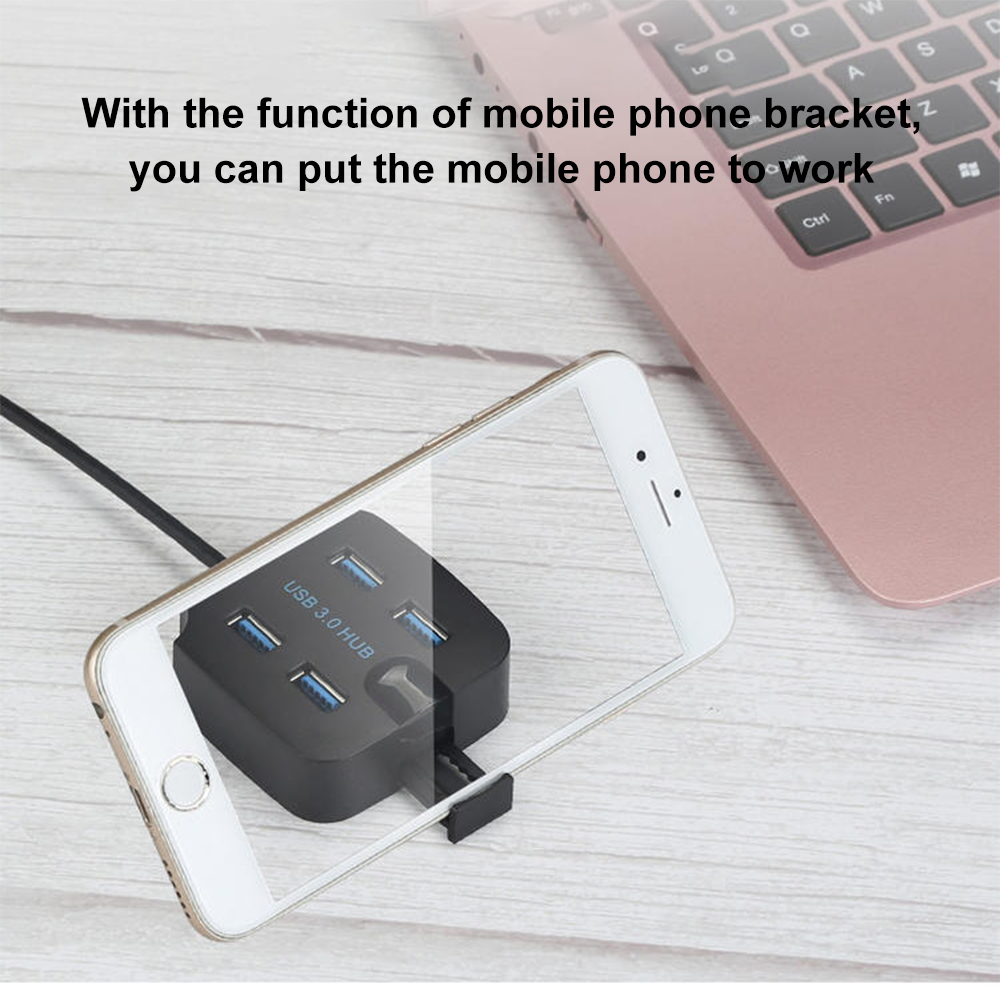Telefon und USB 3.0 Hub auf Holzoberfläche. Telefon dient als Halterung. Rosa Laptop im Hintergrund.