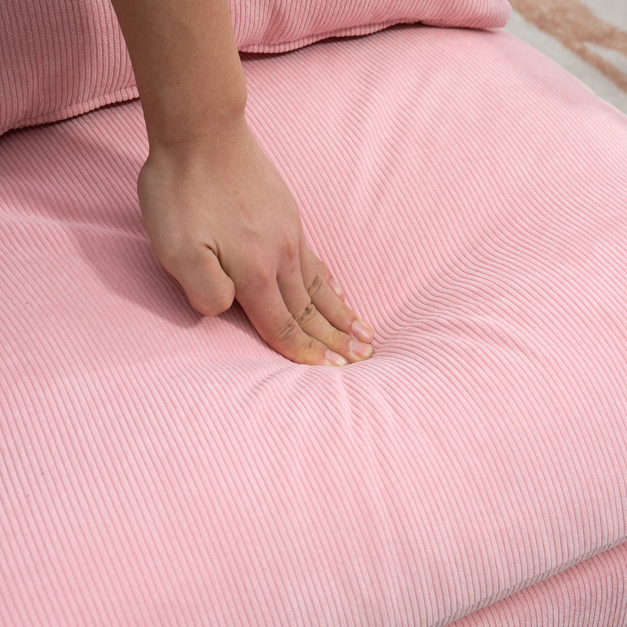 Eine Hand drückt in einen rosa Kordstoff und zeigt die Weichheit.