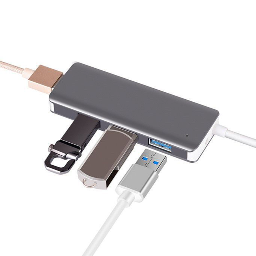 Ein silberner USB-Hub mit angeschlossenen USB-Laufwerken und Kabeln auf weißer Oberfläche.