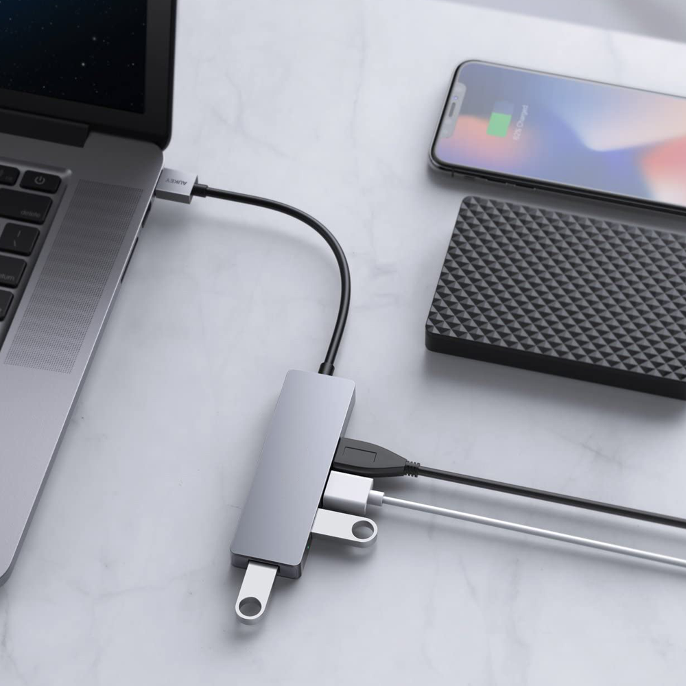 Ein silberner USB-Hub, der an einen Laptop, ein Telefon und eine schwarze externe Festplatte angeschlossen ist.