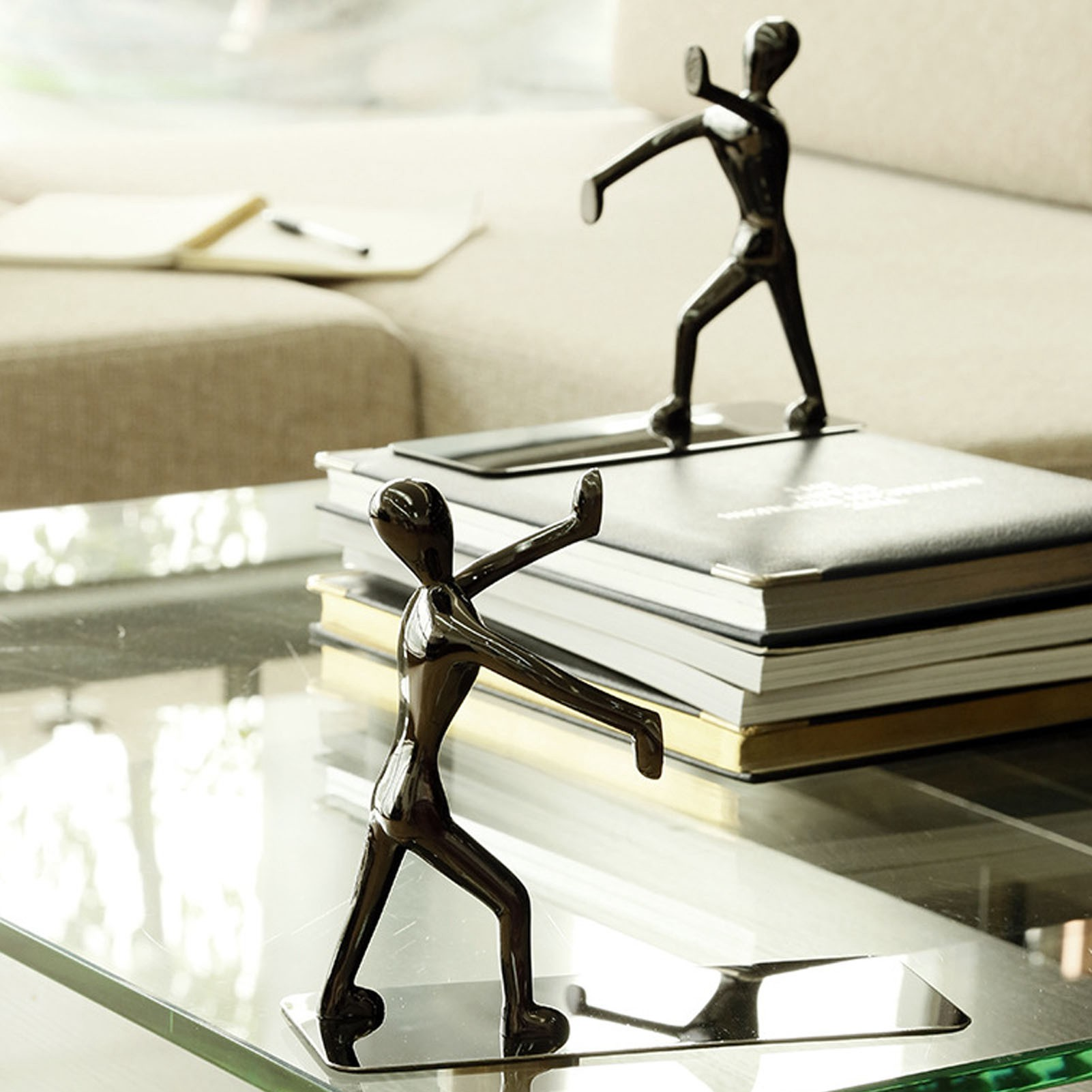 Zwei schwarze Metallfiguren in modernem Ambiente. Eine auf einem Glastisch, die andere auf einem Sofa.