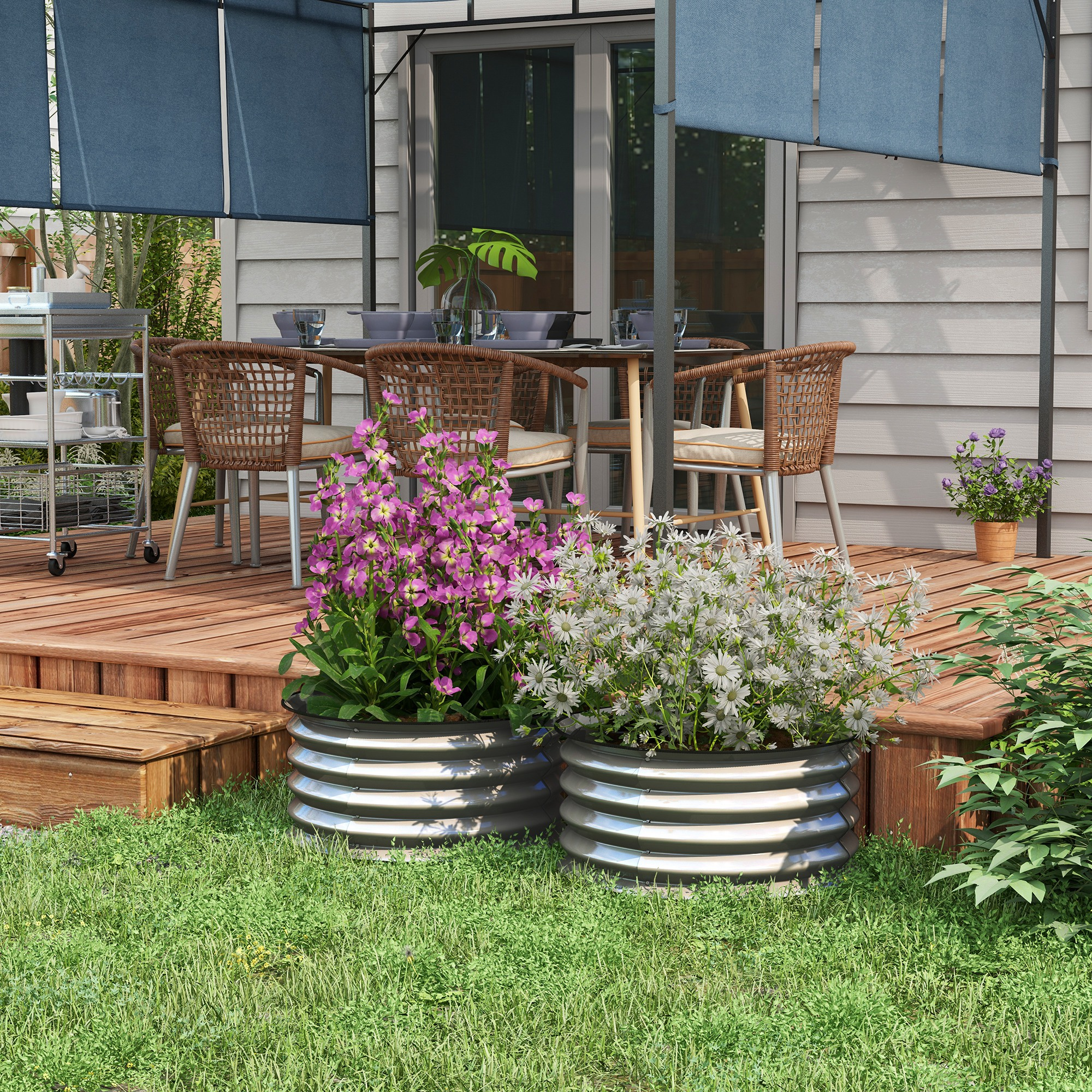 Zwei Metallpflanzer in einem Garten. Sie enthalten Blumen und stehen auf einem Holzdeck. Im Hintergrund ein Haus.