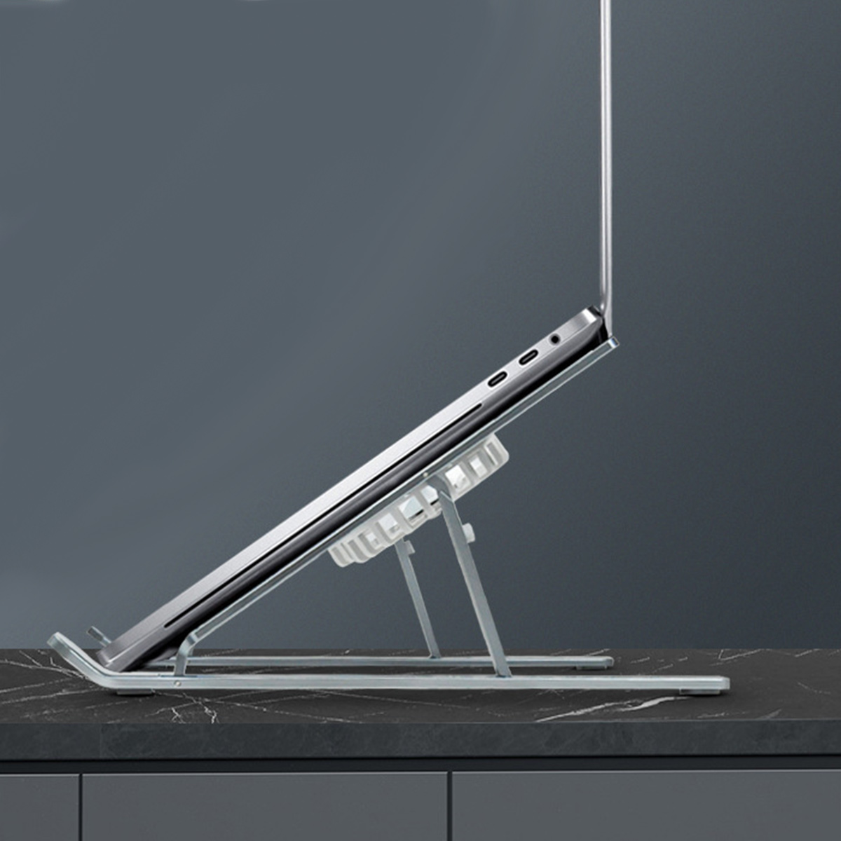 Silberner Laptopständer mit einem Laptop darauf, auf einer schwarzen Oberfläche.