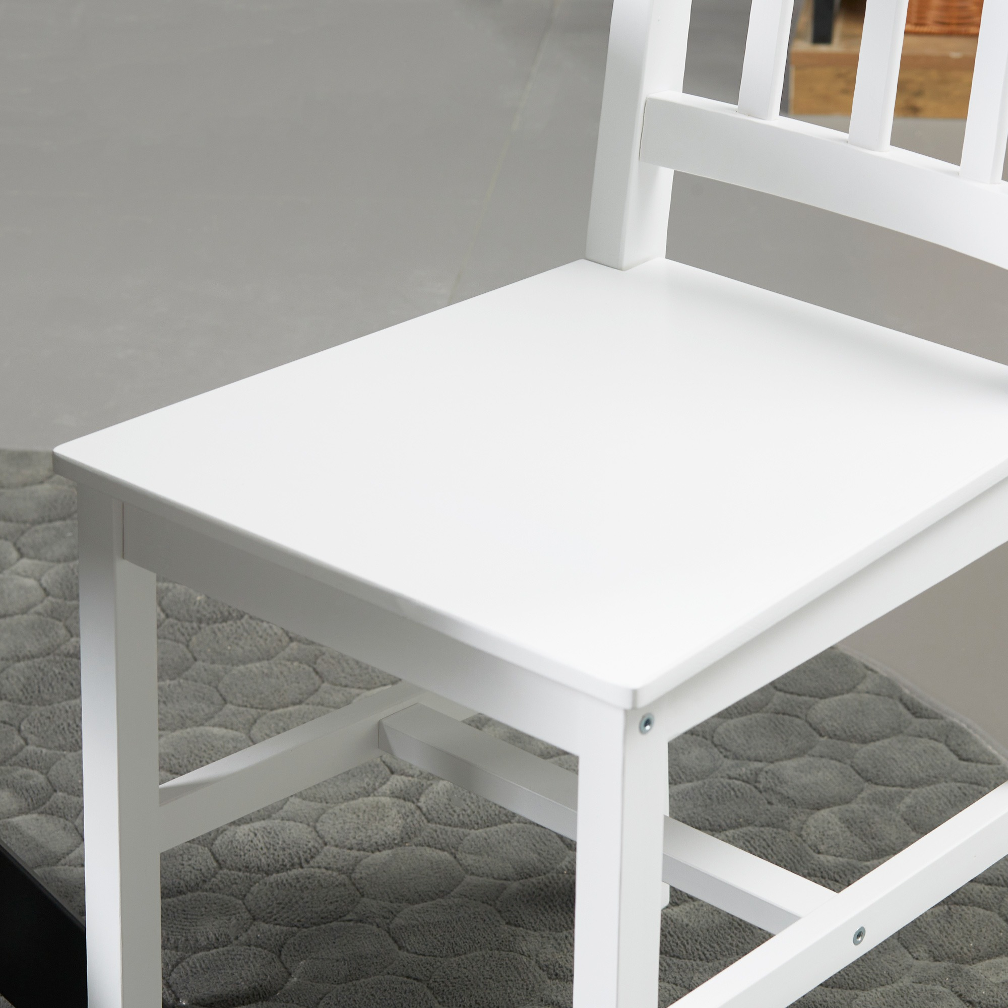 Nahaufnahme von Sitz und Rückenlehne eines weißen Stuhls, einfaches Holzdesign. Auf einem grauen Teppich.