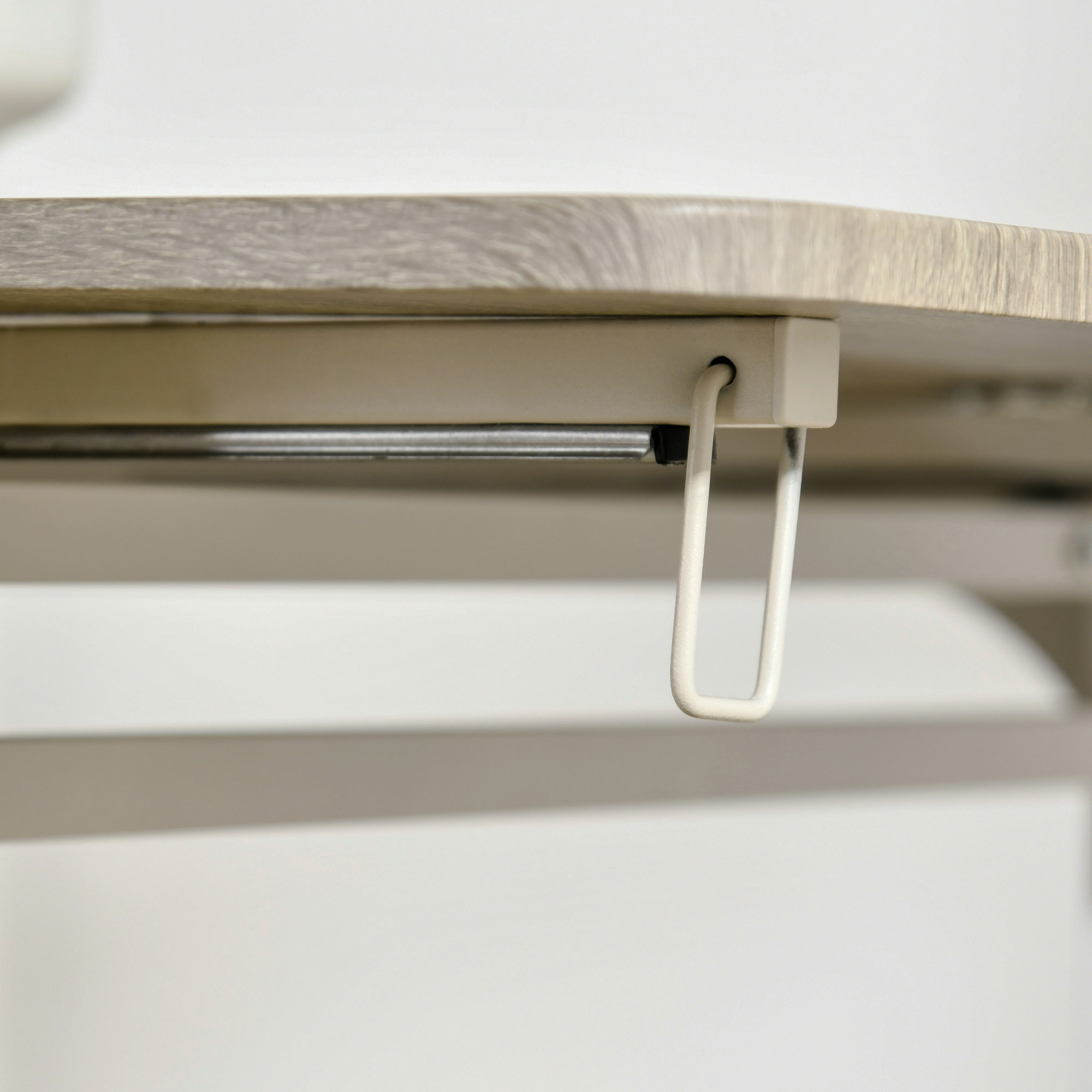 Nahaufnahme der Unterseite eines hellfarbigen Holztisches mit weißer Metallstütze.