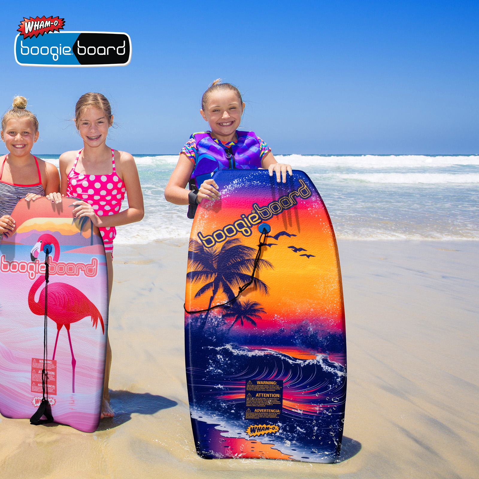 Tre ragazze con boogie board su una spiaggia, oceano sullo sfondo.