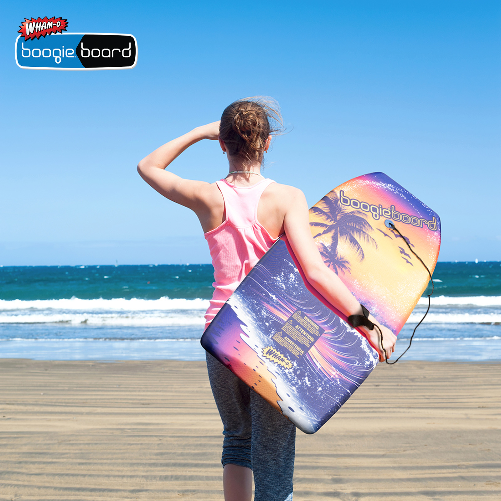 Donna con una tavola da surf sulla spiaggia, che guarda l'oceano sotto un cielo blu. La tavola è blu.