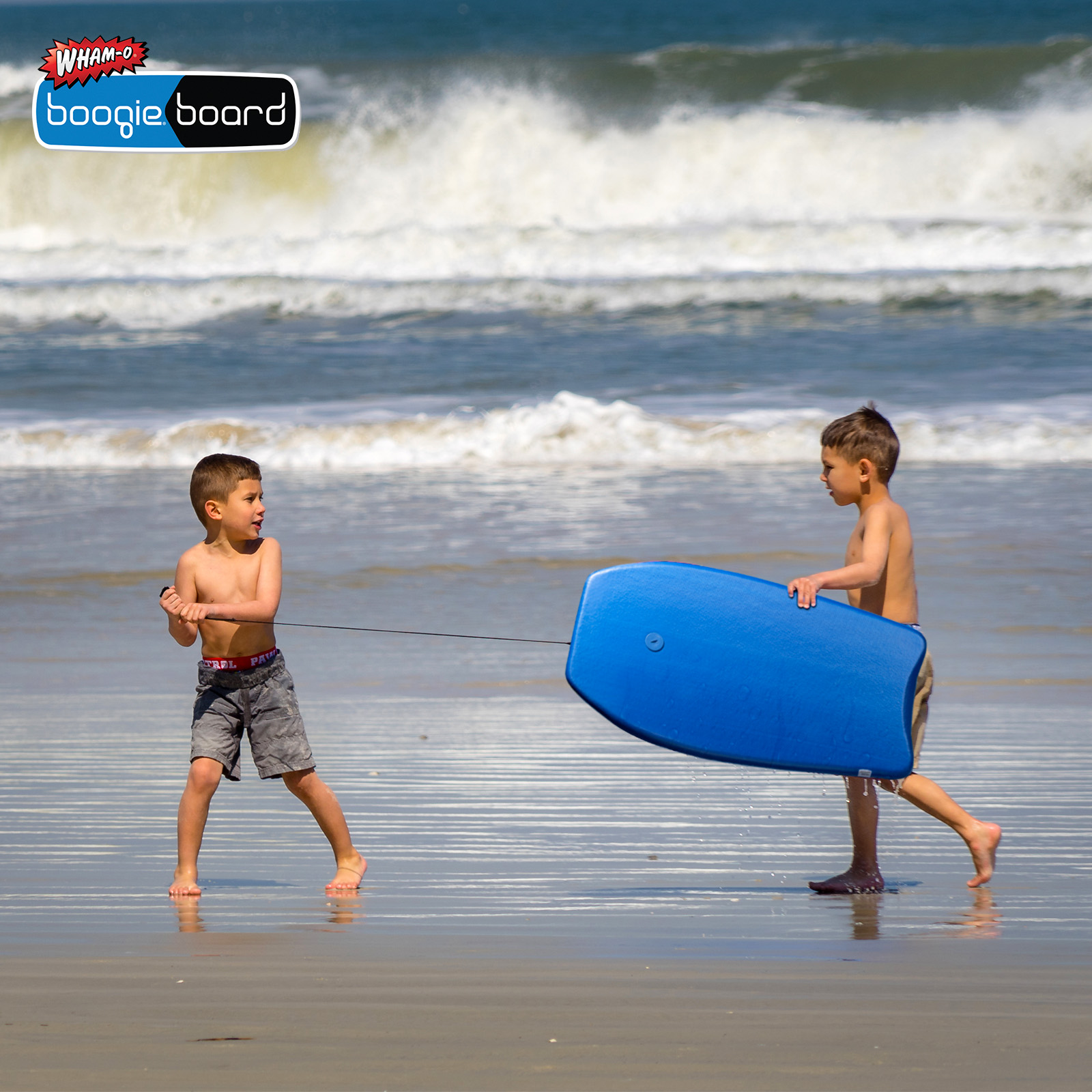 Zwei Jungen am Strand mit einem Boogieboard. Einer zieht. Text: Wham-O Boogieboard.