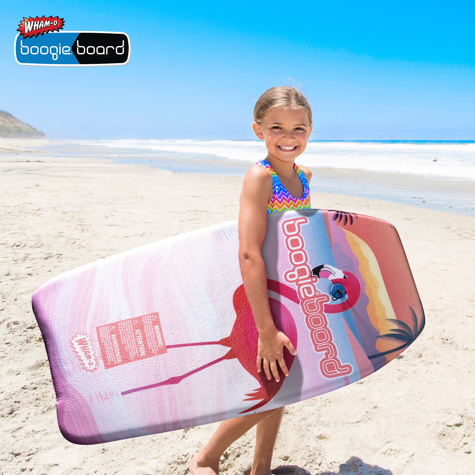 Una ragazza con un boogie board su una spiaggia. La tavola ha un design a fenicottero.