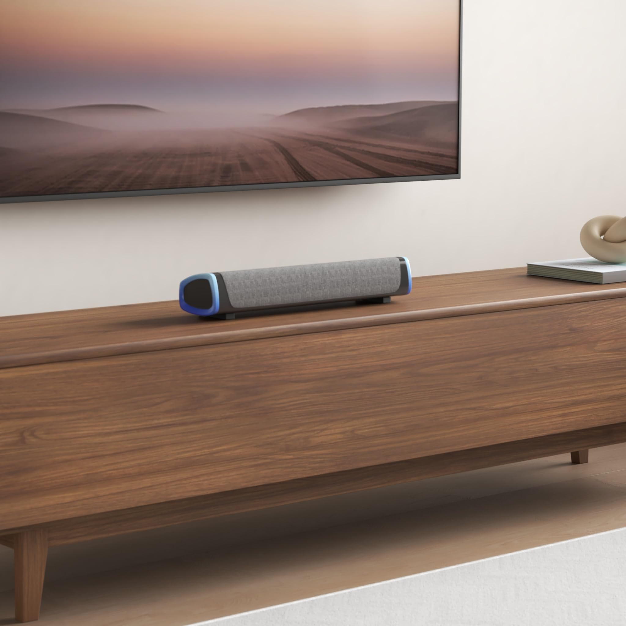 Ein Lautsprecher auf einem Holzschrank vor einem Fernseher, mit einer Berglandschaft im Hintergrund.