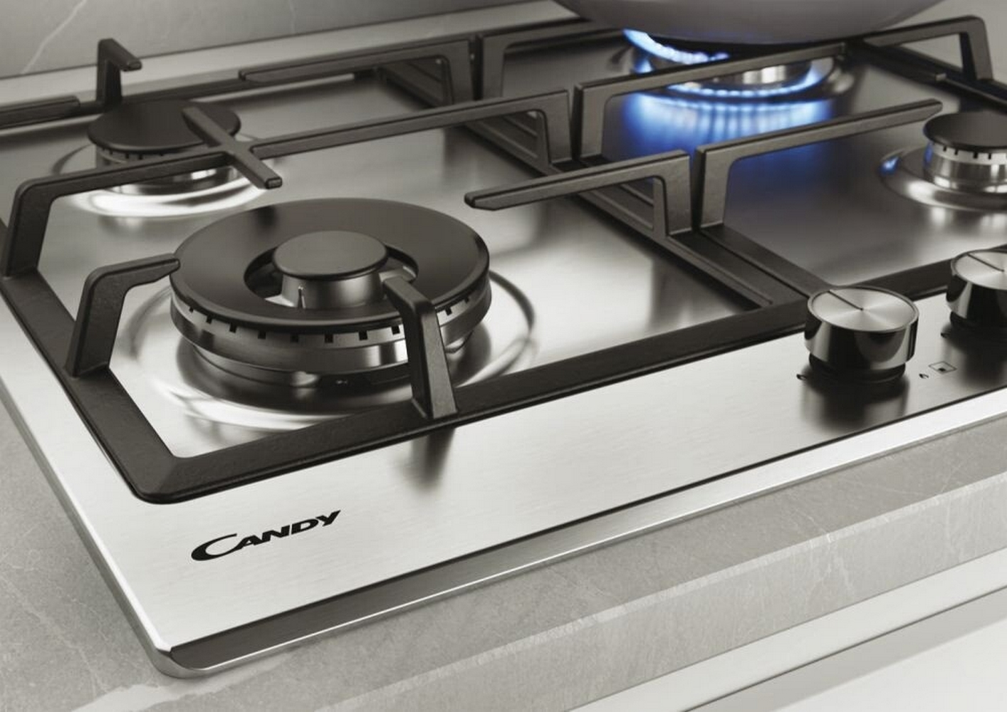 Zbliżenie na gazową płytę grzewczą ze stali nierdzewnej z czterema palnikami i logo Candy.