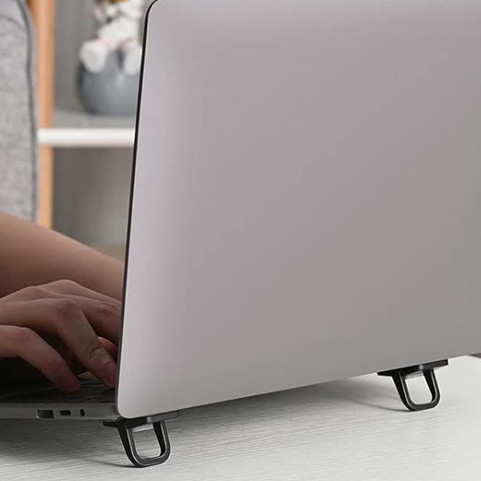 Ein Laptop wird von schwarzen Haken getragen, die an der Unterseite befestigt sind, auf einem weißen Tisch.