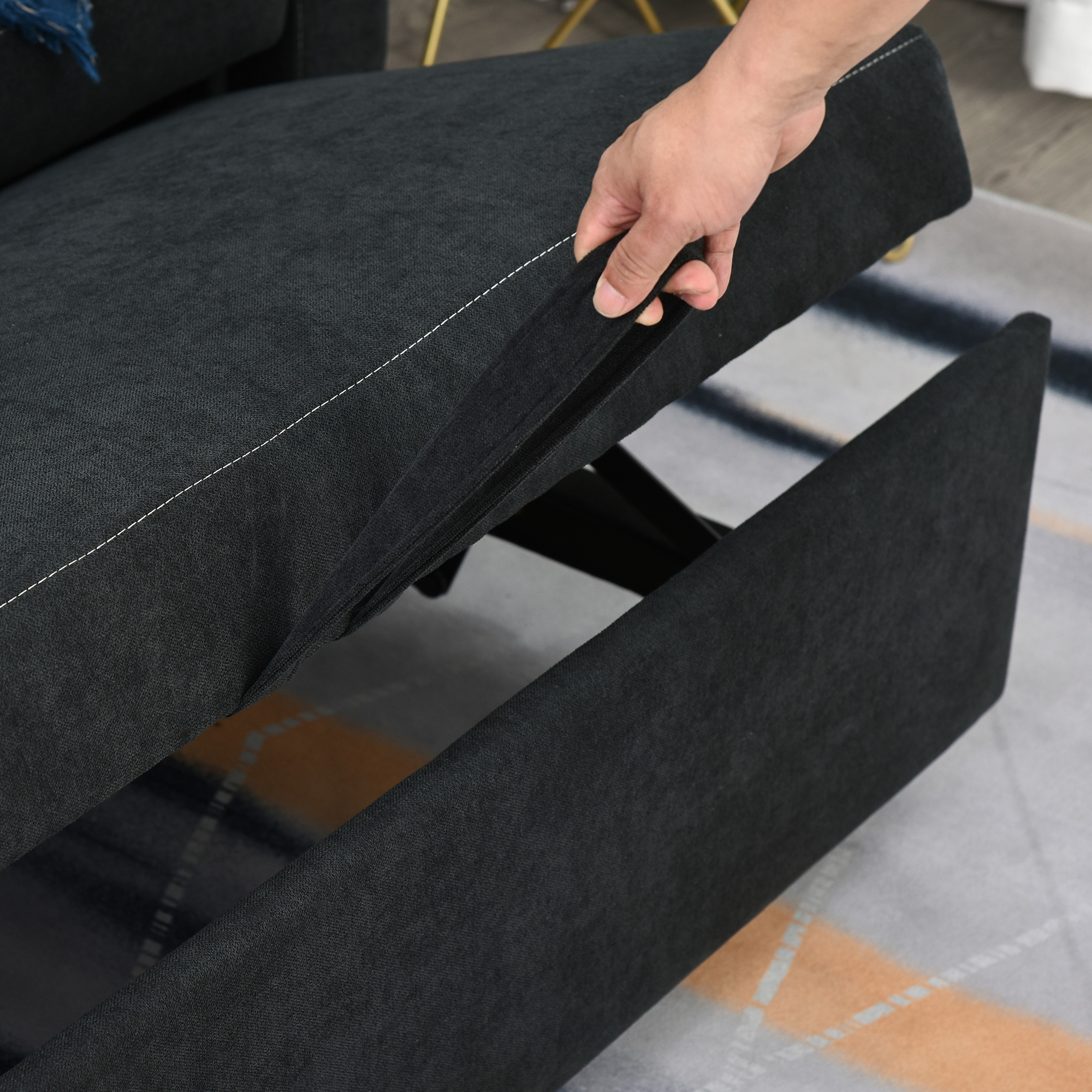 Hand öffnet Schublade unter dunkelgrauem Sofa. Das Innere der Schublade ist sichtbar.
