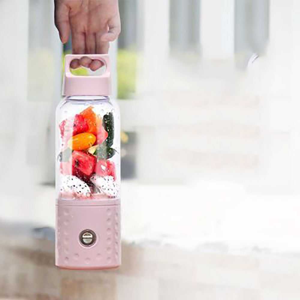 Ein rosa tragbarer Mixer gefüllt mit geschnittenem Obst. Eine Hand hält den Mixer.