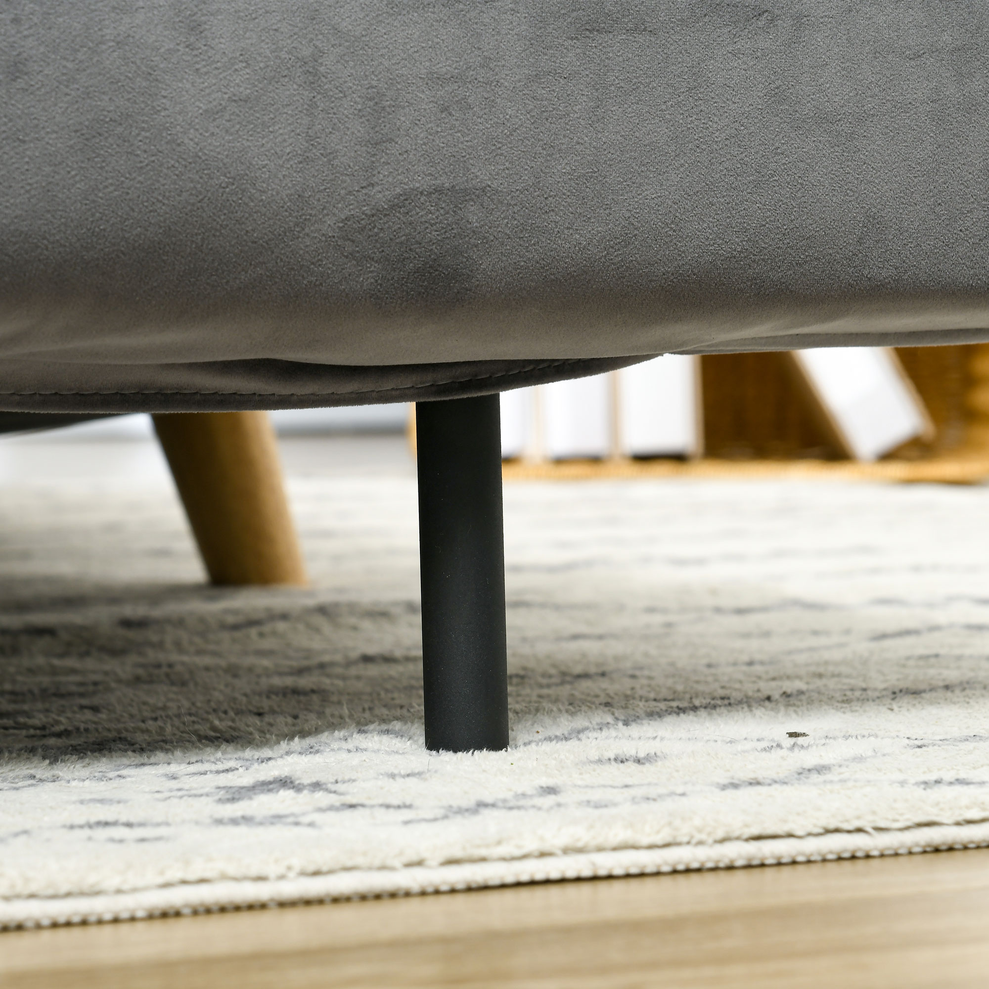 Nahaufnahme der schwarzen Beine eines grauen Sofas auf einem Teppich. Holzbeine links sichtbar.