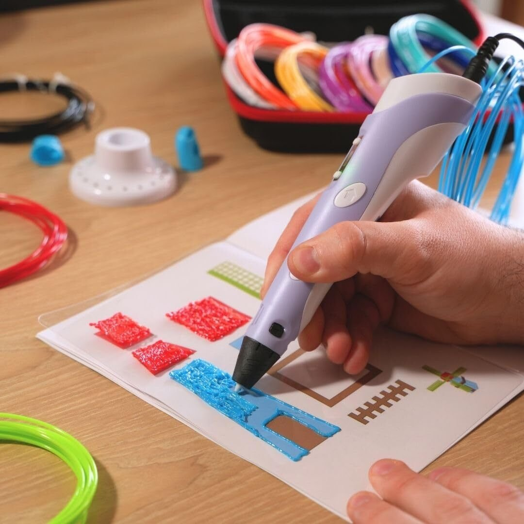 Una persona usa un bolígrafo 3D para dibujar en una página. Varios colores de filamento plástico y accesorios están cerca.