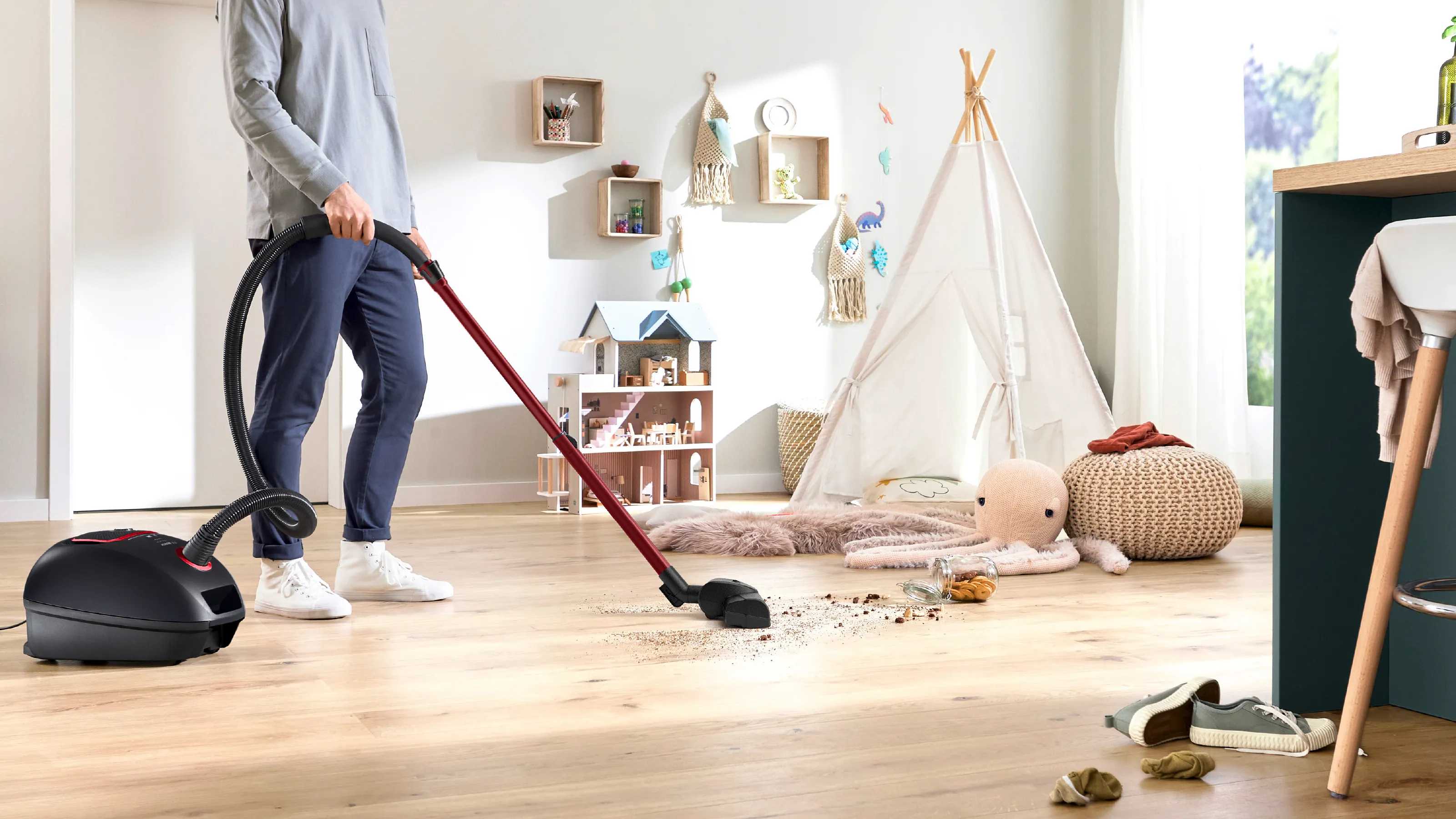 Una persona aspira un piso de madera en una habitación infantil. Una tienda de campaña, juguetes y una casa de muñecas.