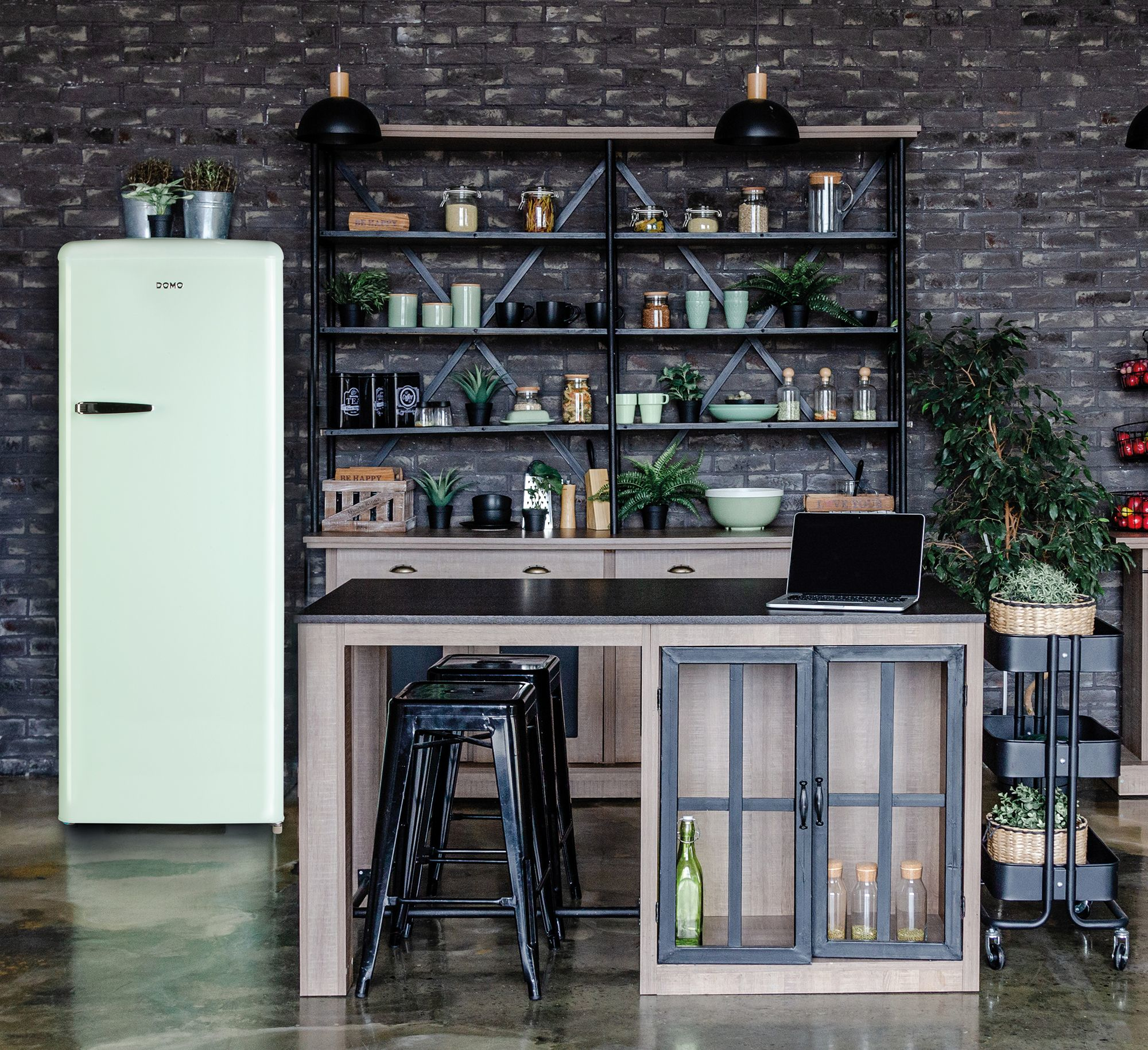 Küche mit grünem Retro-Kühlschrank, Tisch mit Hockern und Backsteinmauer im Hintergrund.