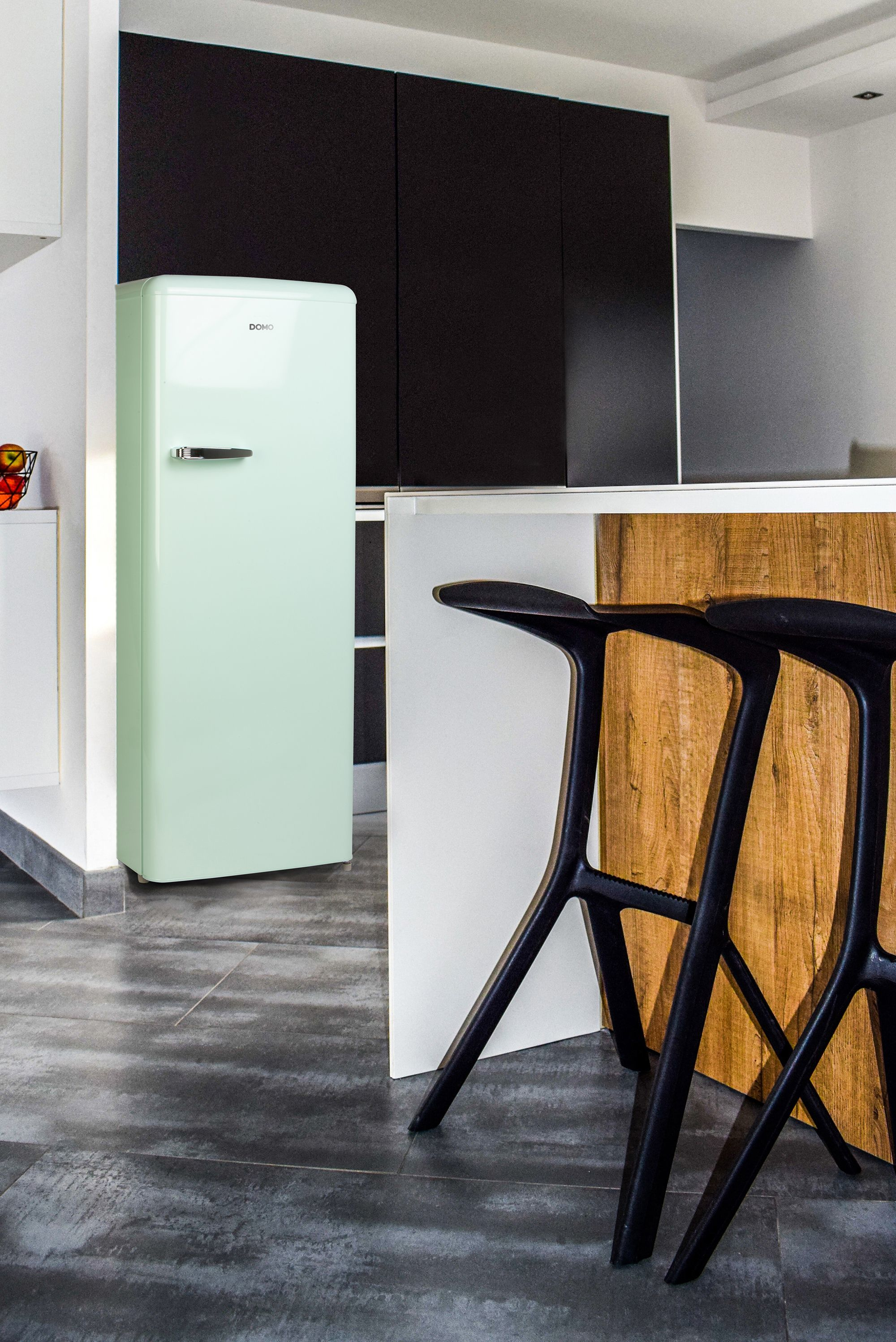 Ein hellgrüner Retro-Kühlschrank in einer Küche. Schwarze Hocker und Schränke sind ebenfalls sichtbar.