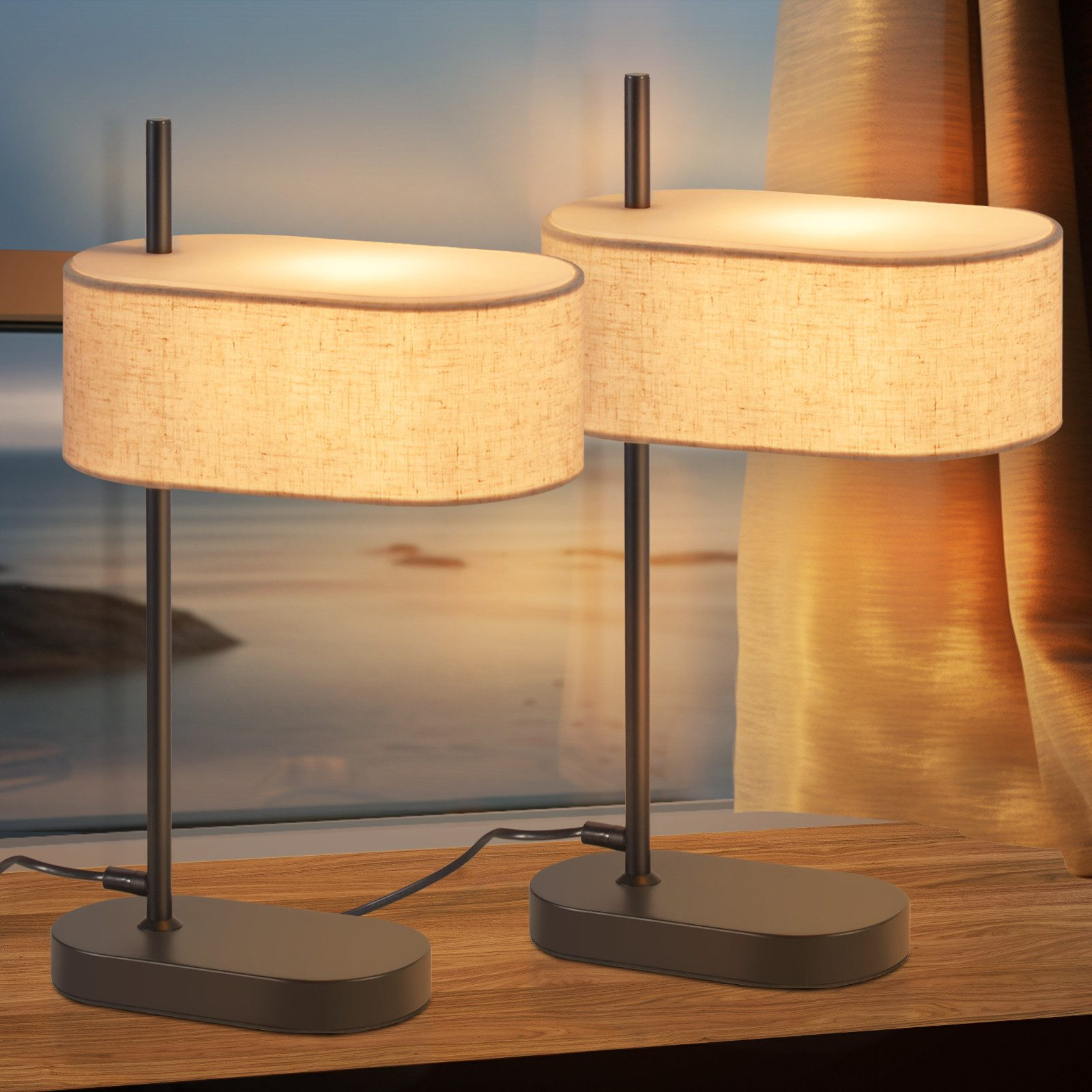 Dwie lampy stoją na drewnianej powierzchni. Mają ciemną podstawę i cylindryczny, beżowy klosz.
