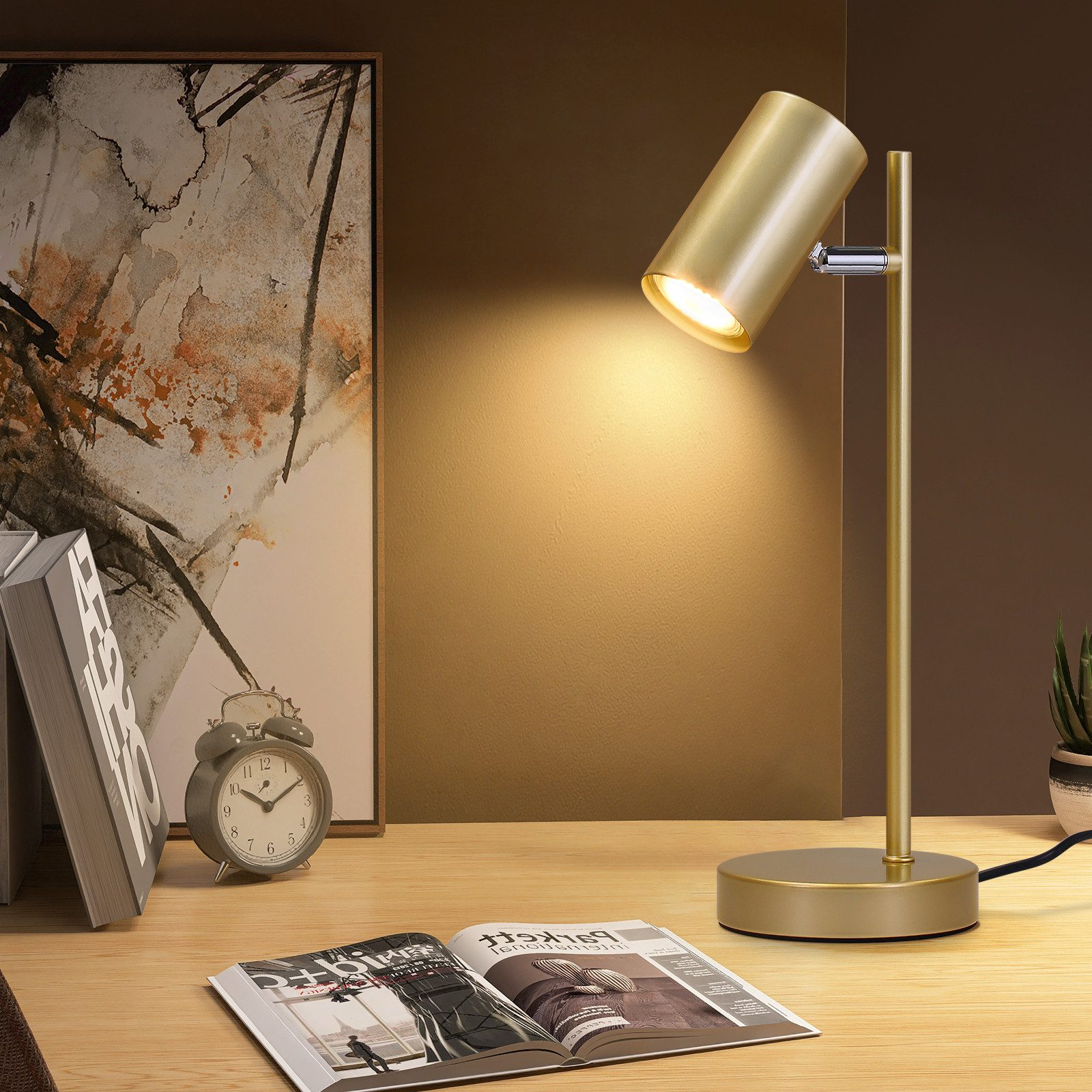 Złota lampa na drewnianym biurku. Książka, budzik i obraz również na biurku.