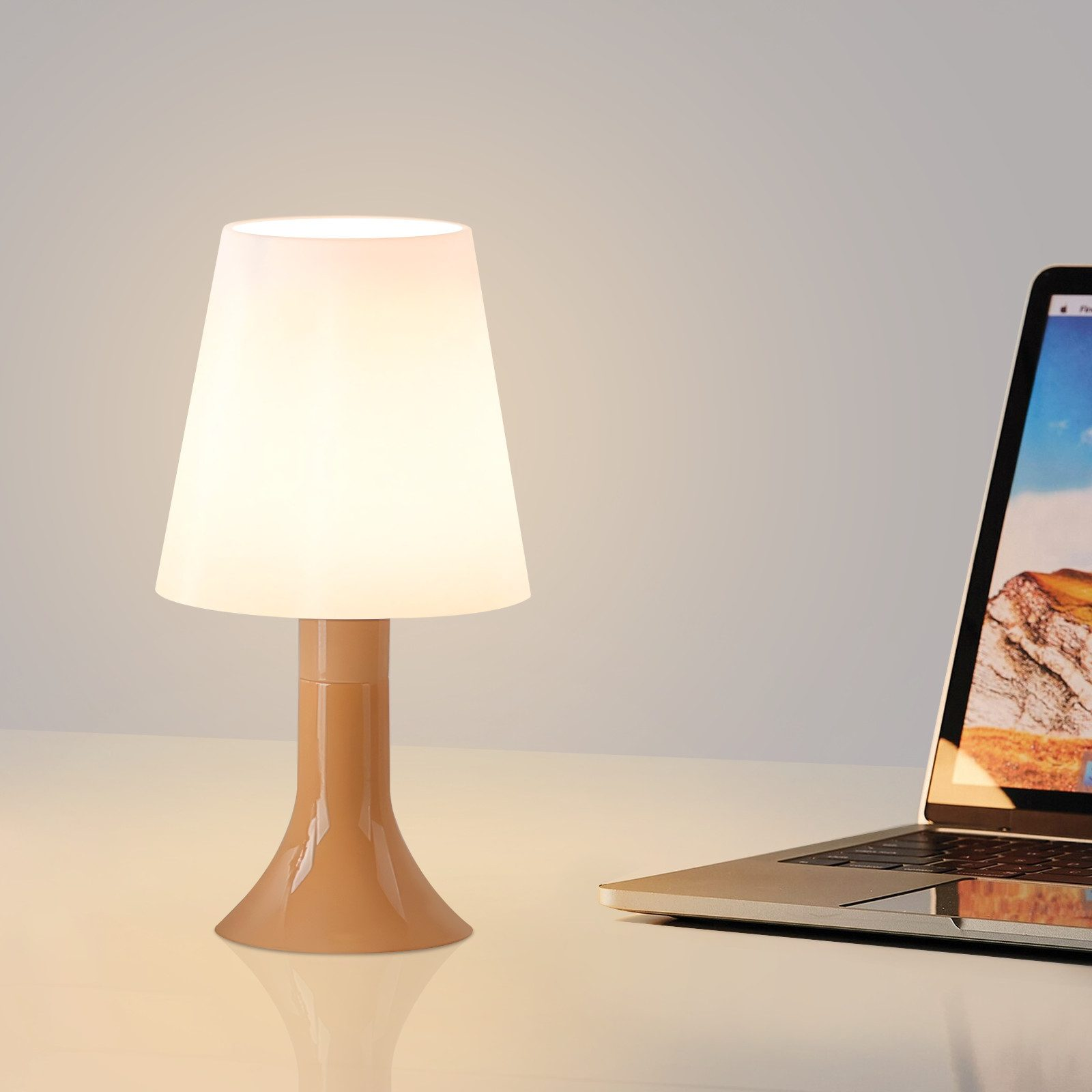 Lampada da tavolo con base beige e paralume bianco. Un laptop è posizionato sul lato destro.