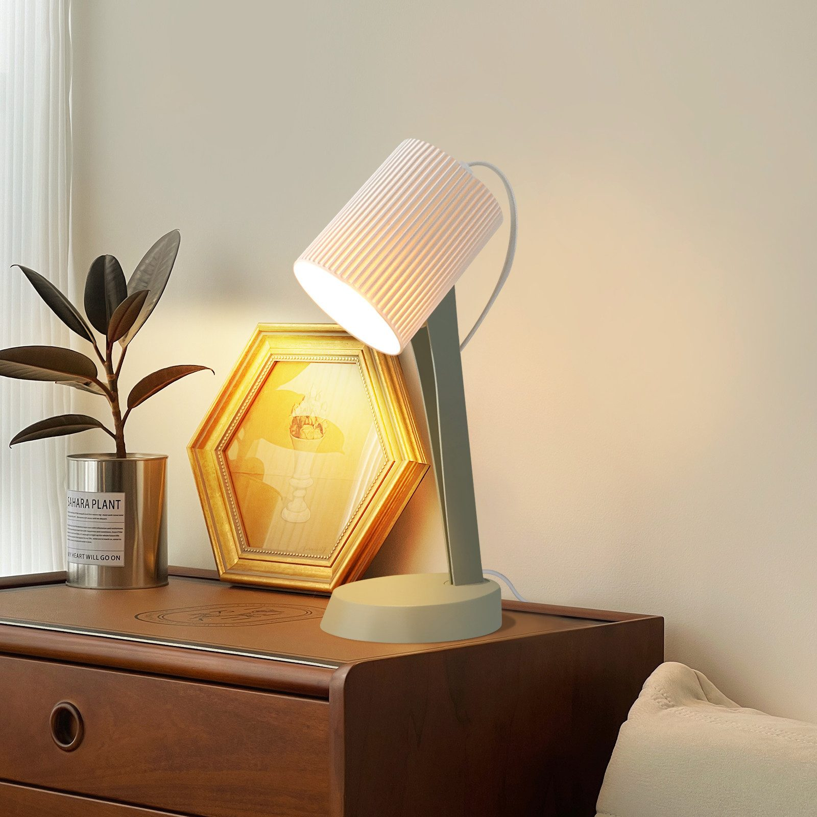 Lampa z białym kloszem i drewniany stół z rośliną i ramką na zdjęcia.